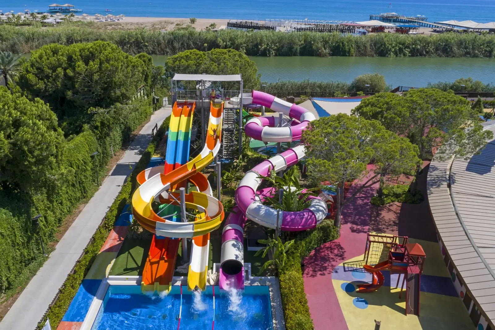 Uitzicht op een waterspeeltuin met glijbanen en waterattracties, omgeven door groen bomen, met de oceaan en stranden op de achtergrond.