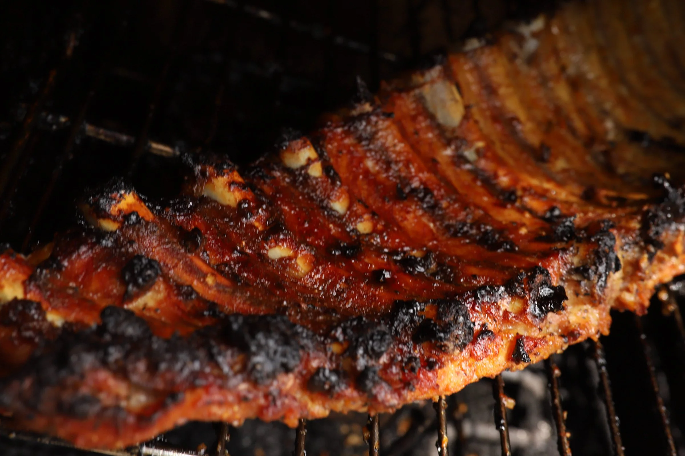 Close-up of a rack of barbecued ribs with a glaze and charred spots on a grill.