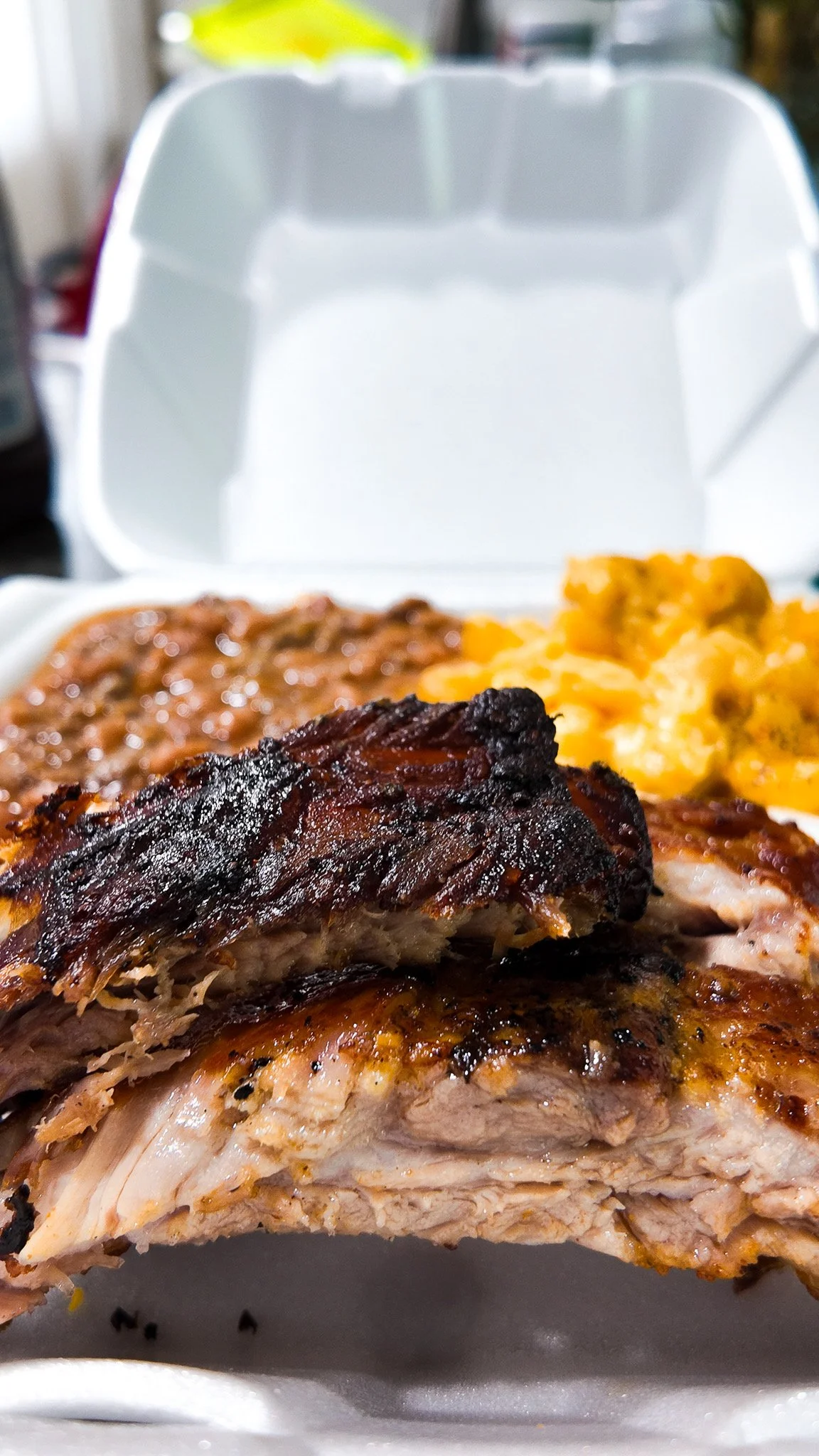 Close-up of smoked, grilled ribs and baked macaroni and cheese in a takeout container.