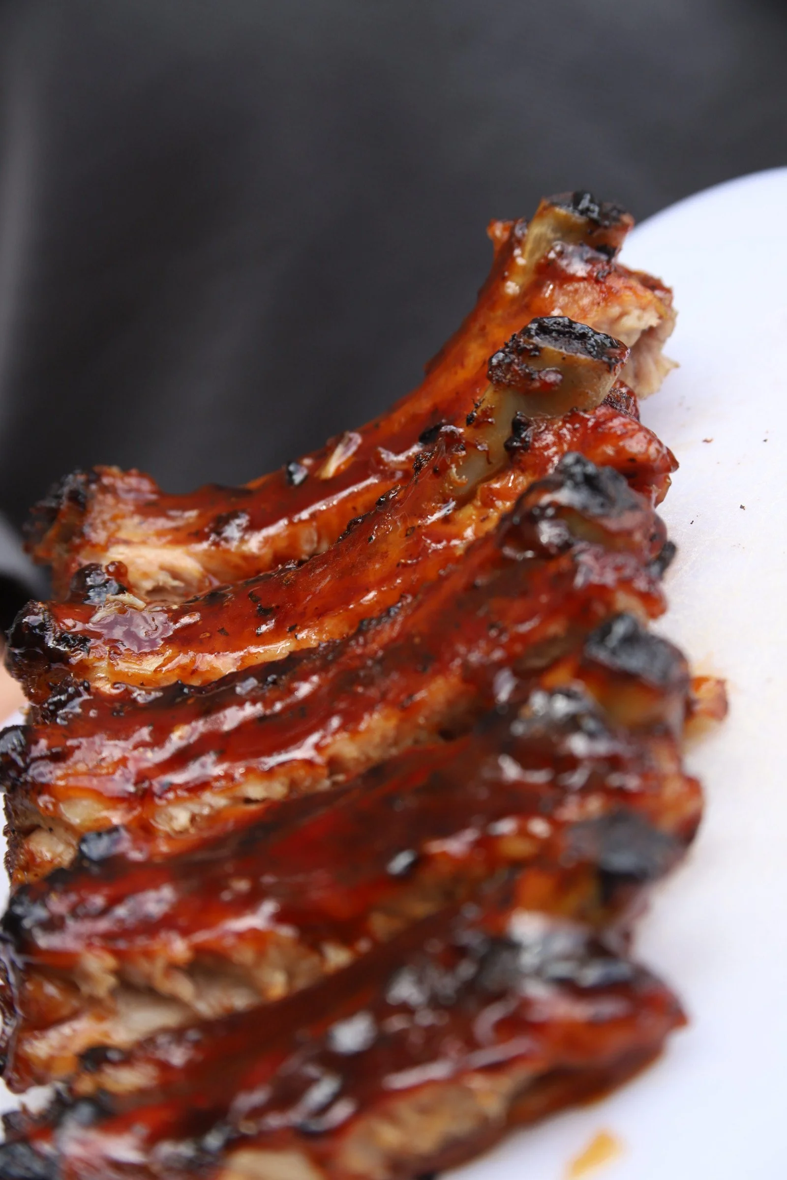 Close-up of a glazed grilled pork rib with caramelized edges, served on a white plate with a dark background.