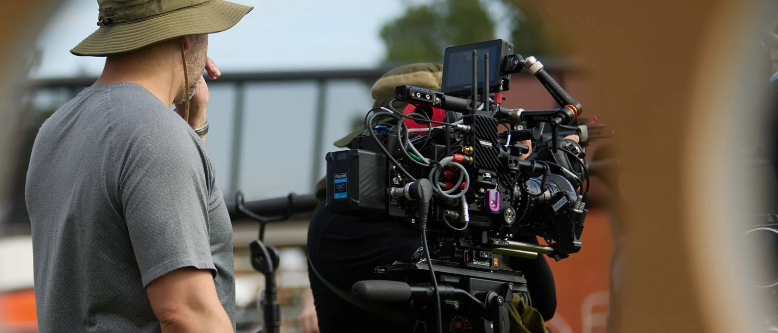 Crew member operating a professional film camera outdoors on a sunny day.