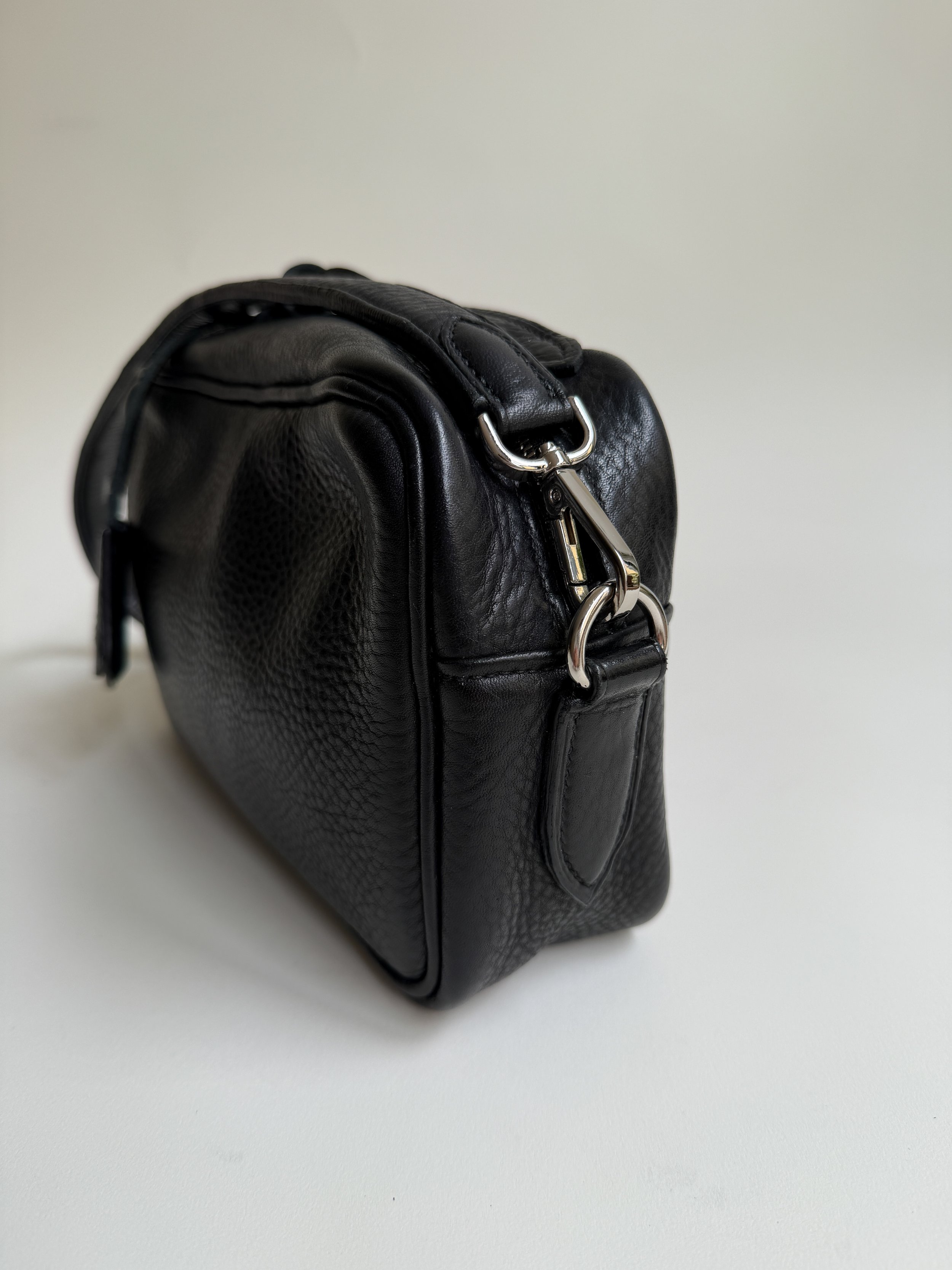 Close-up of a black leather purse with metal hardware on a white surface.