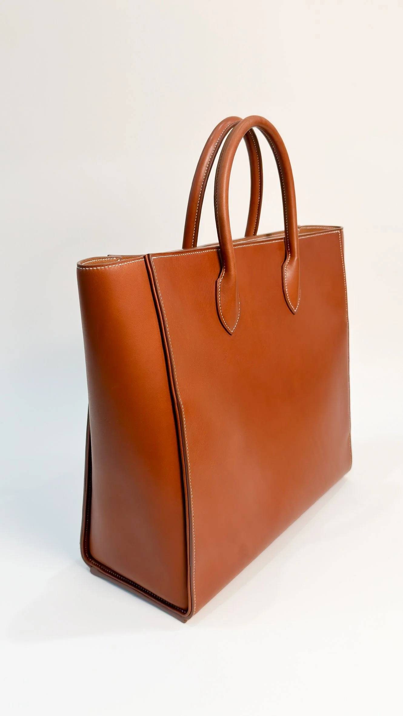 A brown leather tote bag with double handles on a white background.