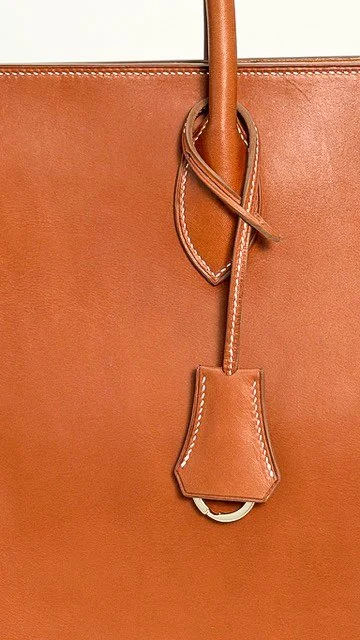 Close-up of a tan leather handbag with a strap and decorative leather tag.