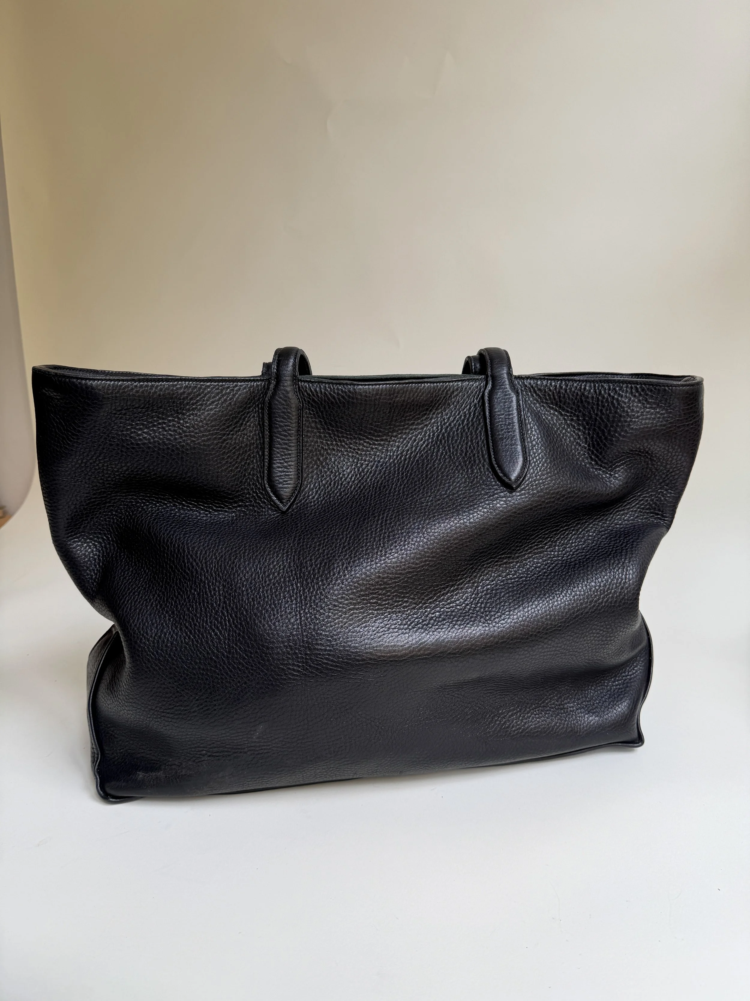 A large black leather handbag with a textured surface, sitting on a white surface against a plain light-colored wall.