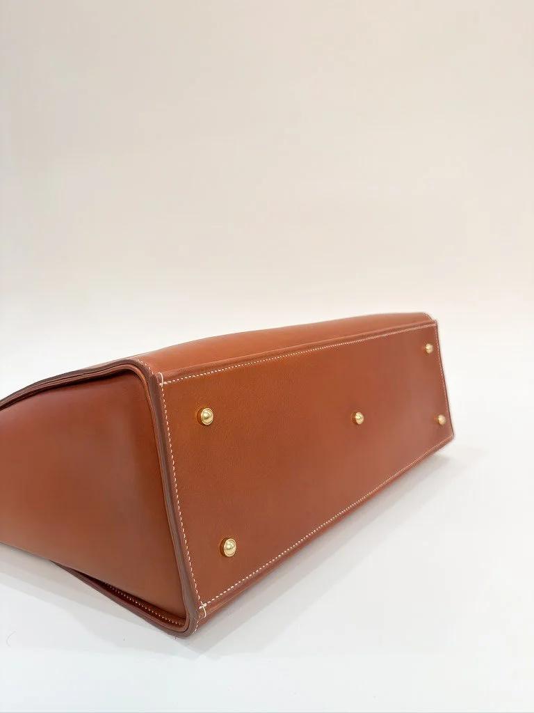 Close-up of a brown leather handbag bottom with gold metal feet on a white surface.