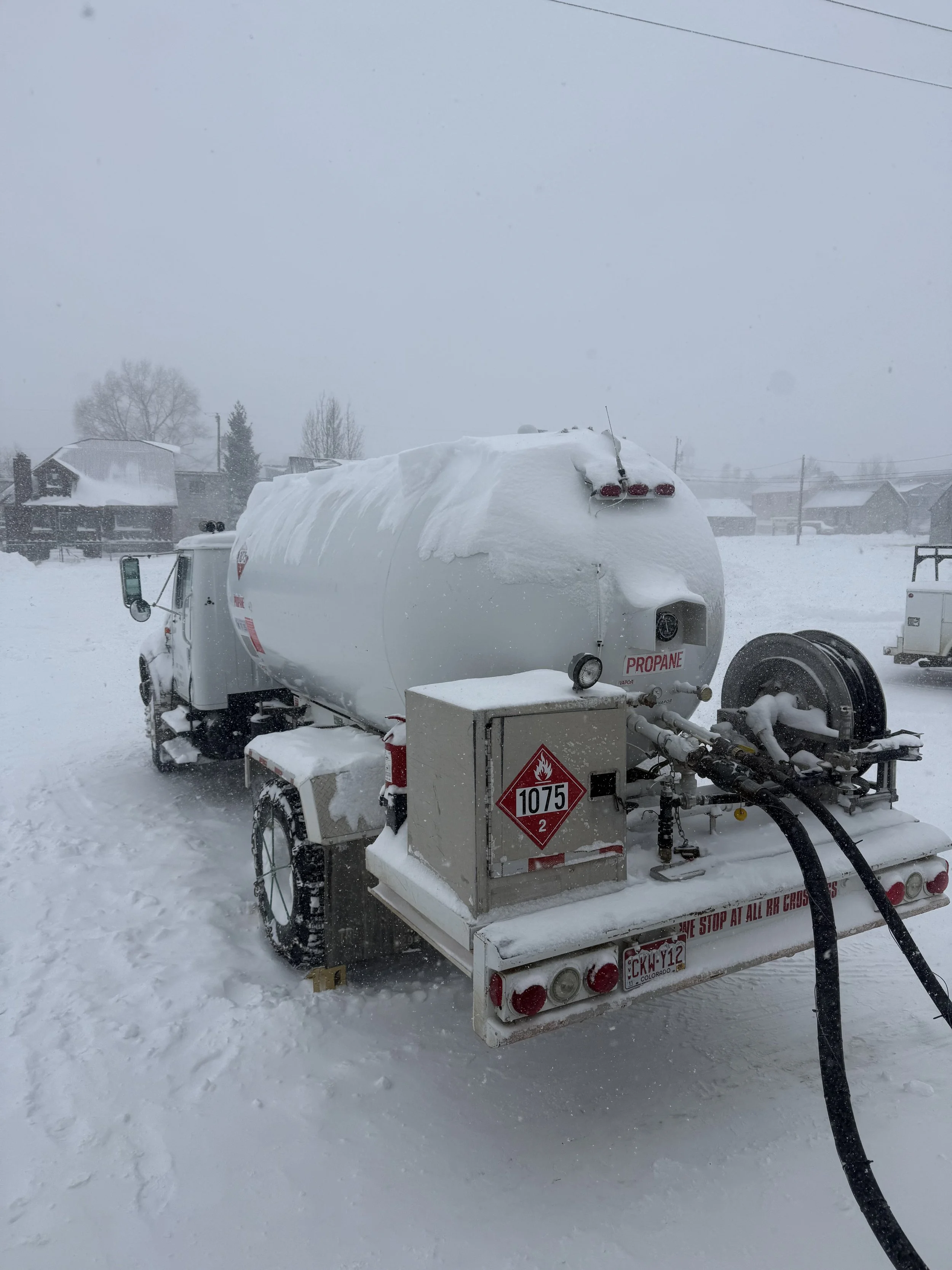 A snow-covered propane tank on a trailer in a snowy landscape with houses and trees in the background.