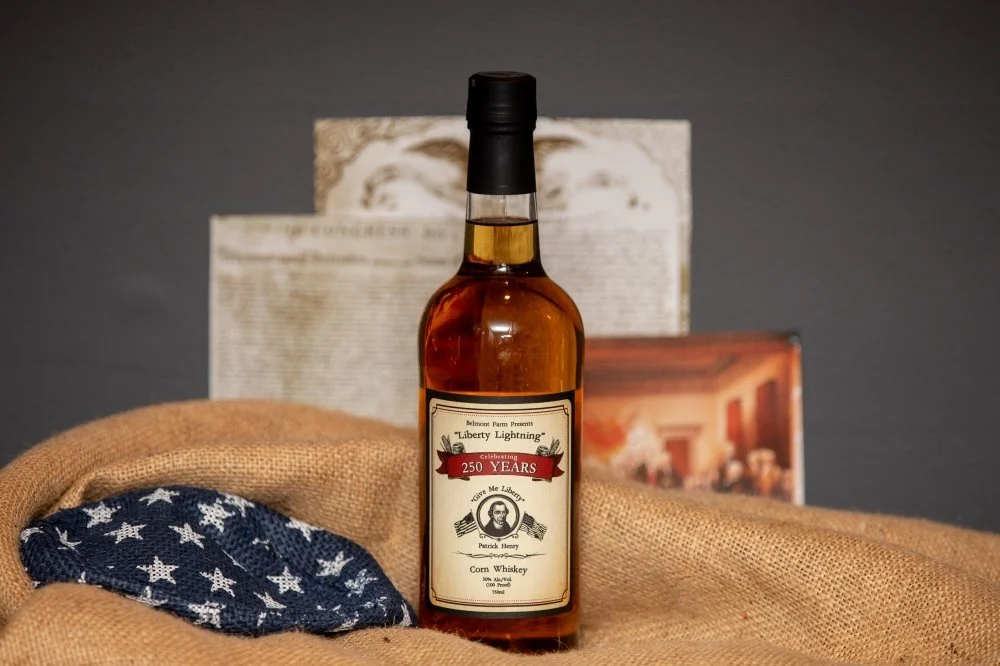 A bottle of whiskey with a label celebrating 250 years, placed on burlap fabric alongside a folded American flag and historical documents in the background.