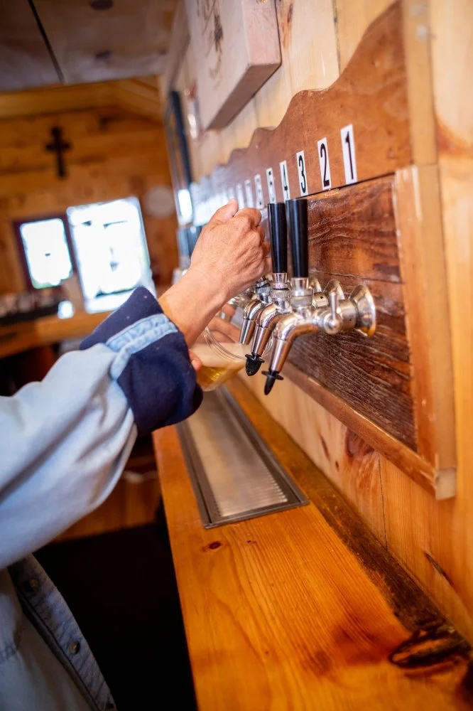 A person pouring beer from tap handles labeled 1, 2, 3, and 4 at a wooden bar or brewery.