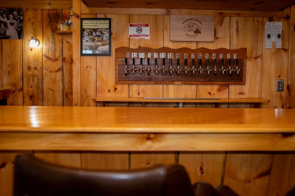 A row of 15 beer taps numbered from 1 to 15, mounted on a wooden wall in a rustic bar setting.