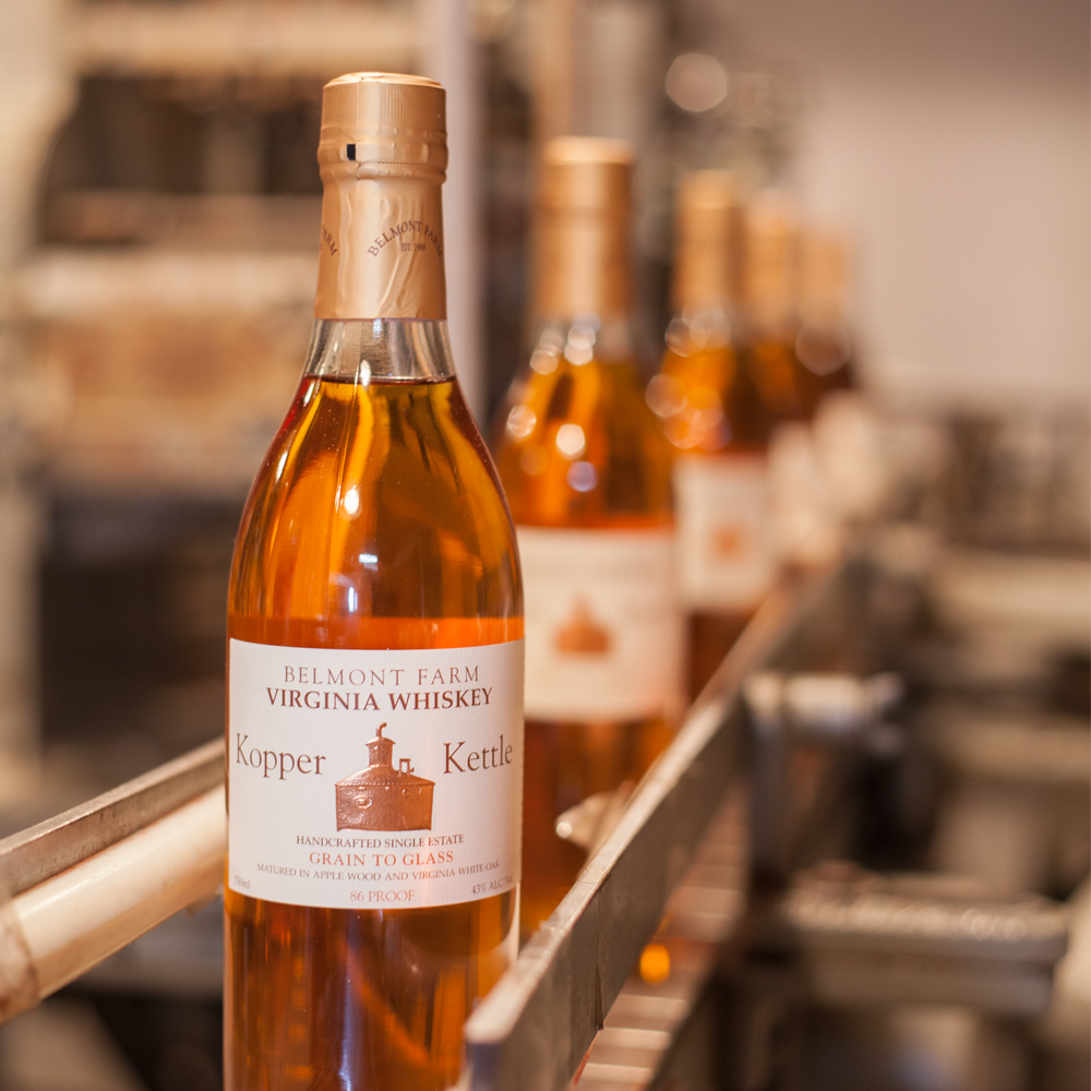 Bottle of Belmont Farm Virginia Whiskey labeled 'Kopper Kettle' on a production line.