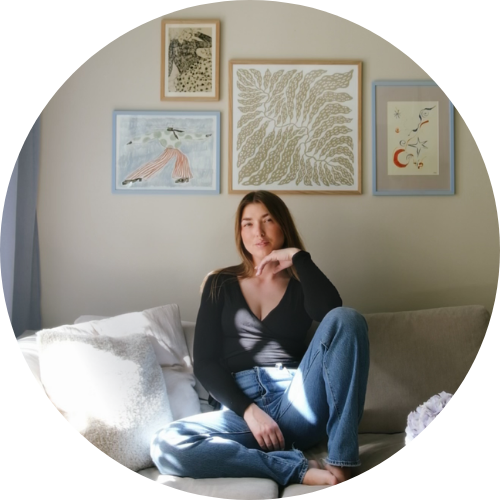 A woman sitting on a sofa in a well-lit room with framed artwork on the wall behind her.