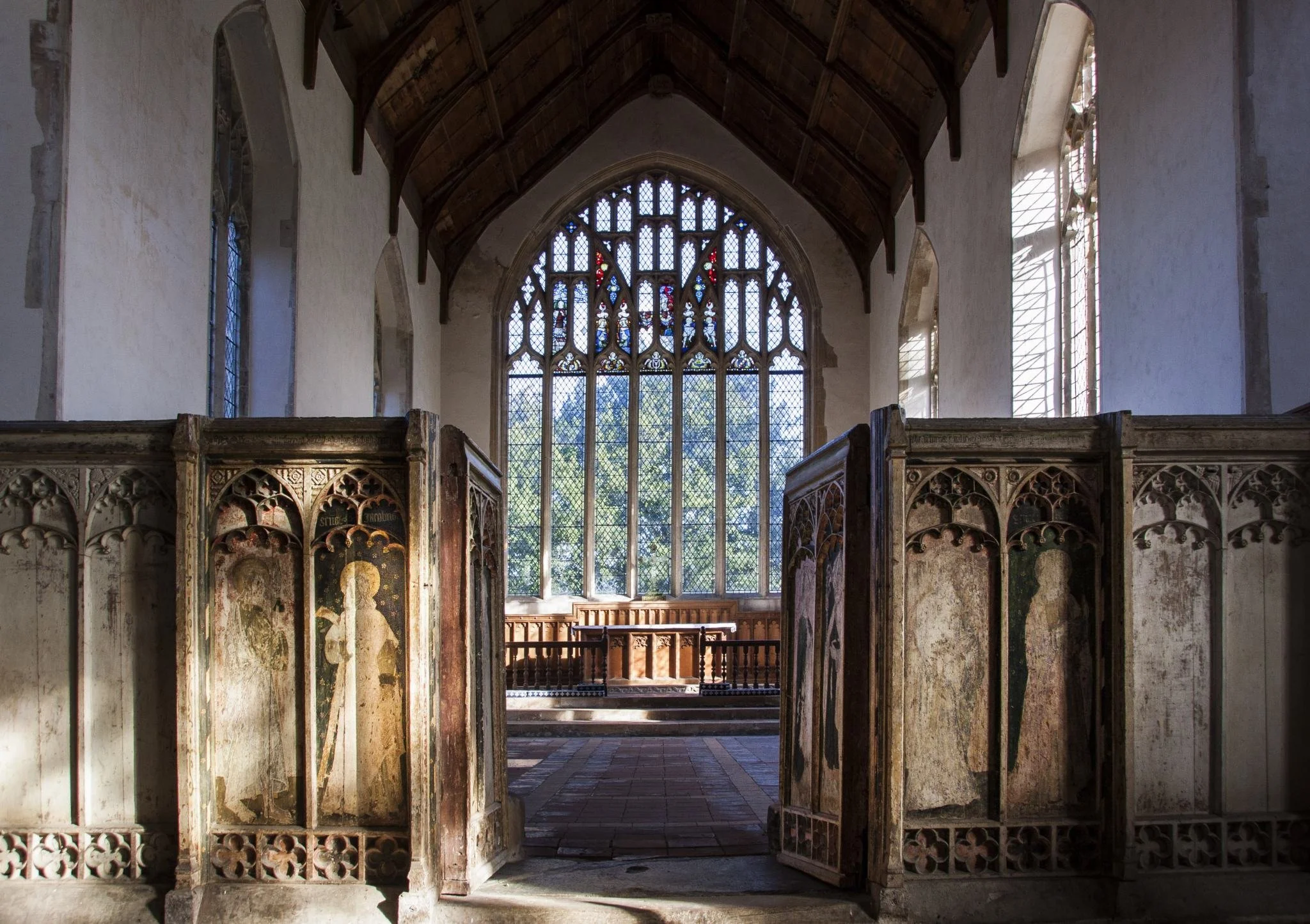 Inside view of an old church with stained glass windows, high wooden ceiling, and decorative wood carvings on both sides.