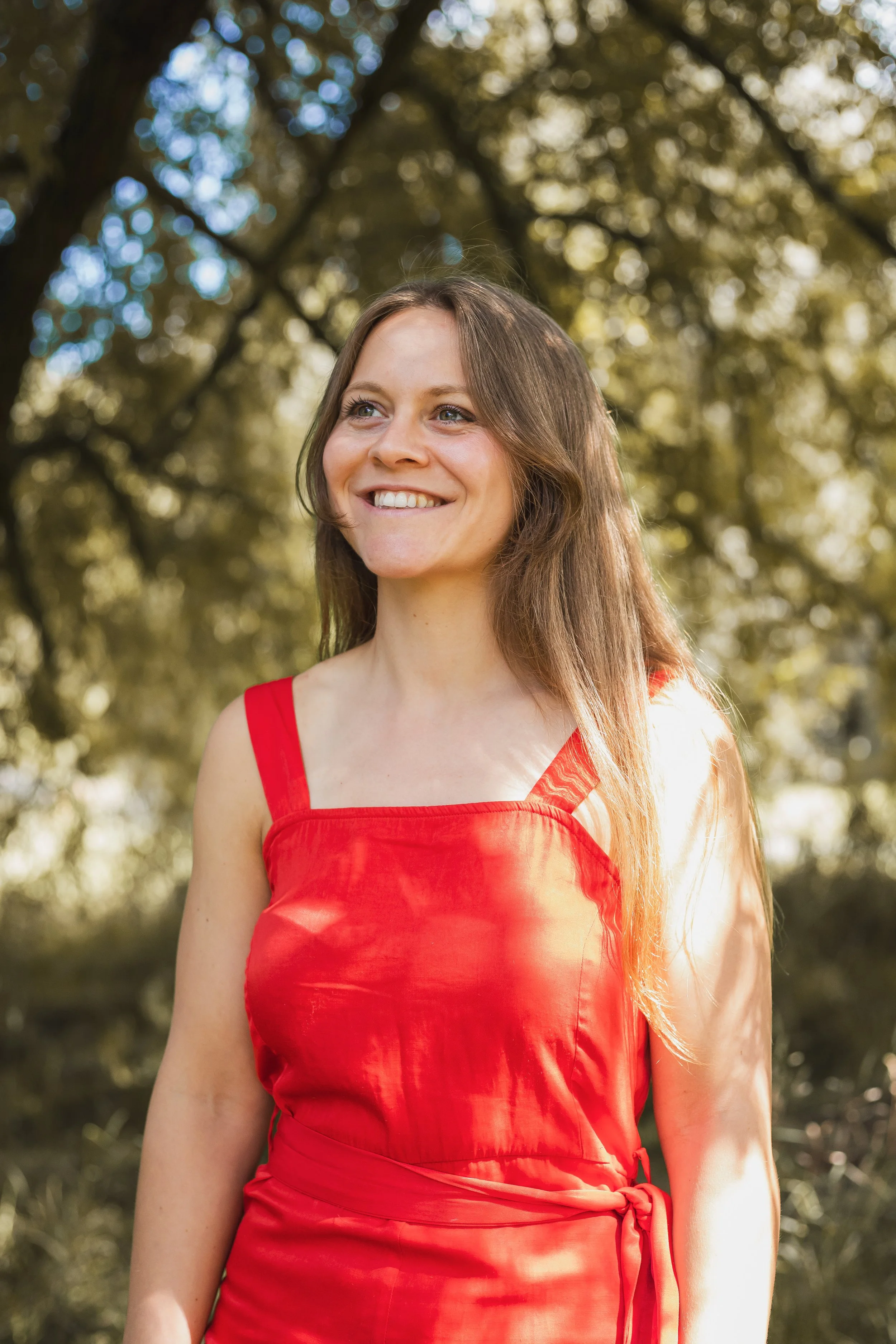 A woman smiling in an outdoor setting wearing a red dress.