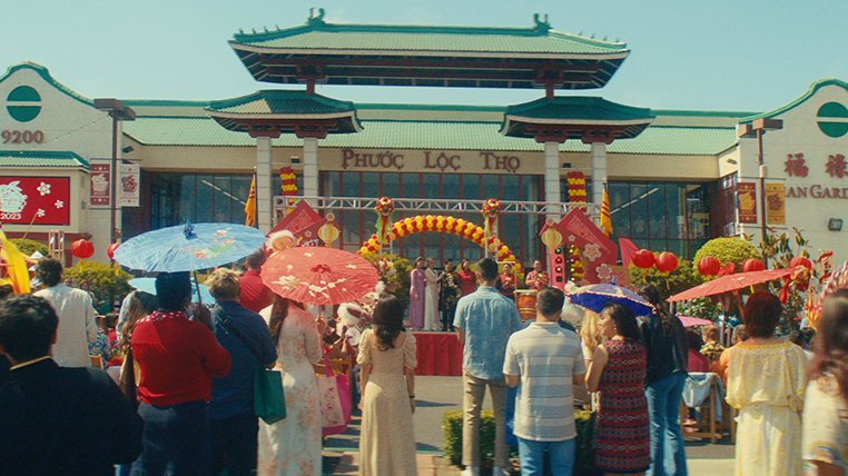 Crowd gathered at a Chinese cultural event with a backdrop of a traditional Chinese building, decorated with red lanterns, balloons, and banners.