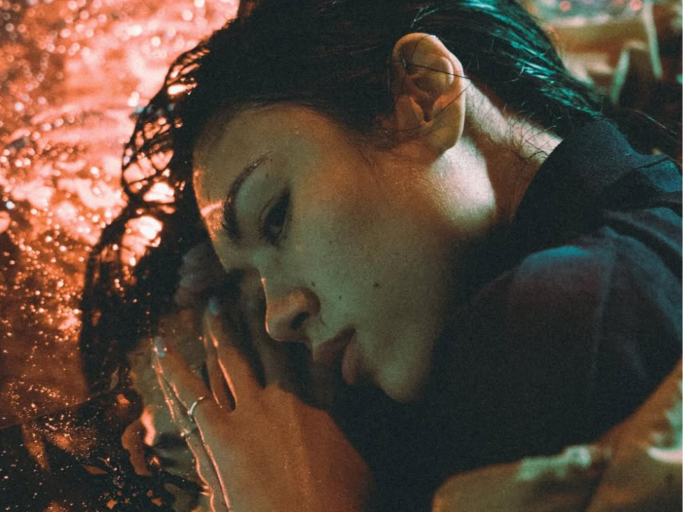 Close-up of a woman with wet hair lying on a reflective surface with colorful, glowing lights.