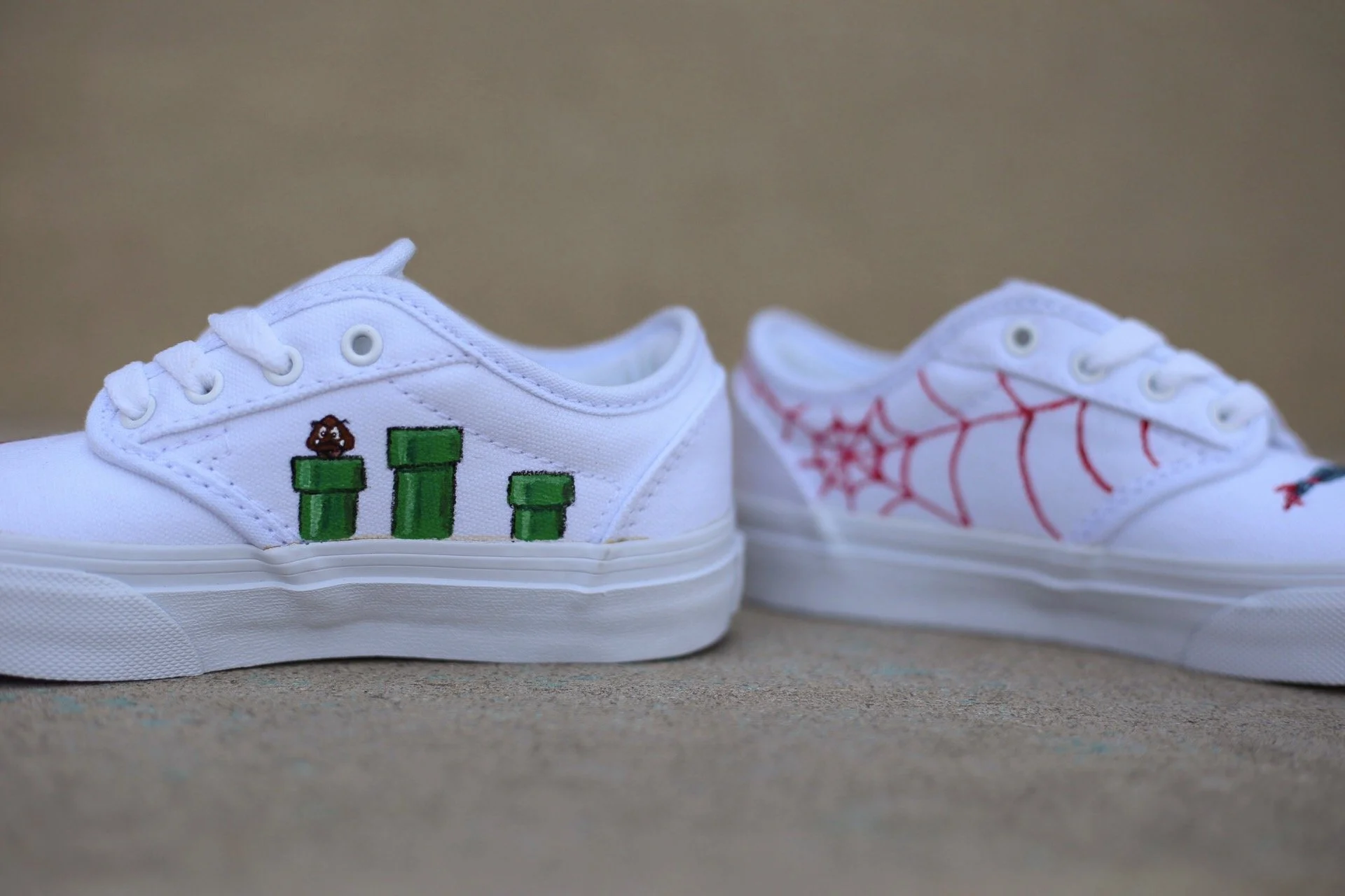 Pair of white sneakers, one with hand painted Super Mario elements and the other with red spiderman design.
