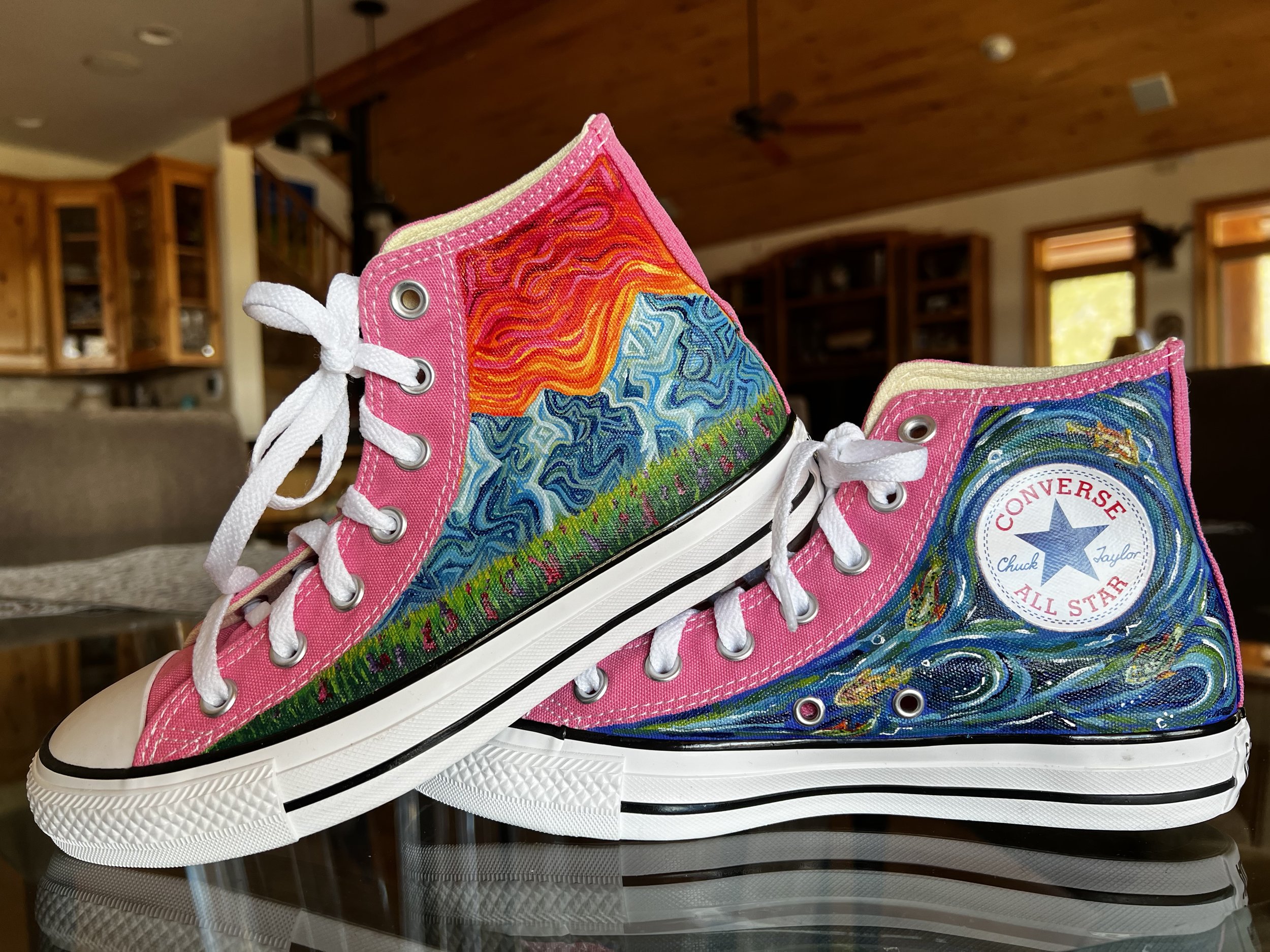Close-up of colorful pink high-top Converse sneakers with vibrant, swirling mountains on the side, and fish swimming in a river. 