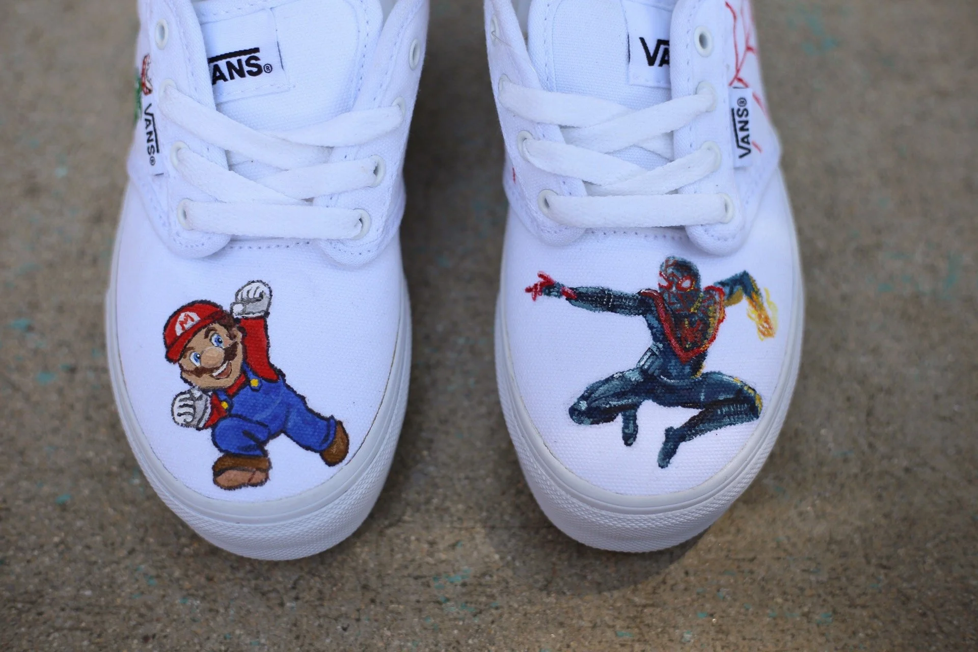 White sneakers with hand-painted characters: Mario on the left shoe and a fighter from Super Smash Bros. on the right shoe, and spiderman on the left shoe. 