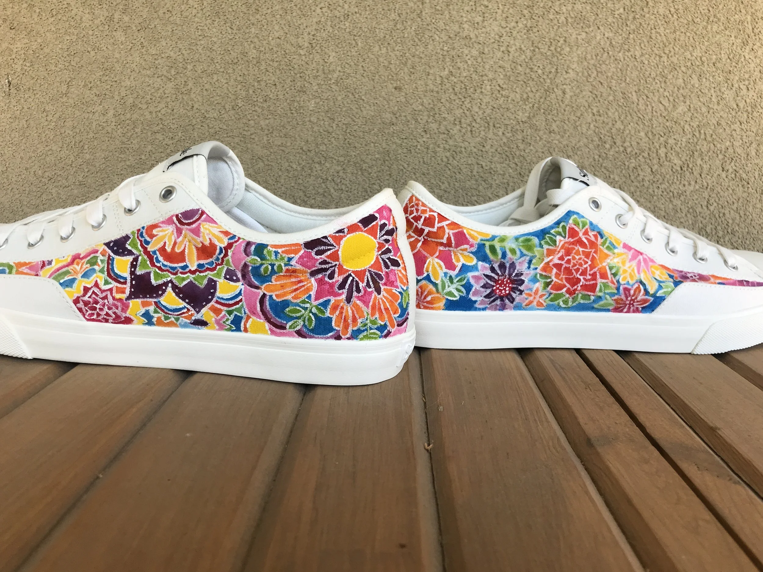 Pair of white sneakers hand painted with colorful floral patterns on the sides. 