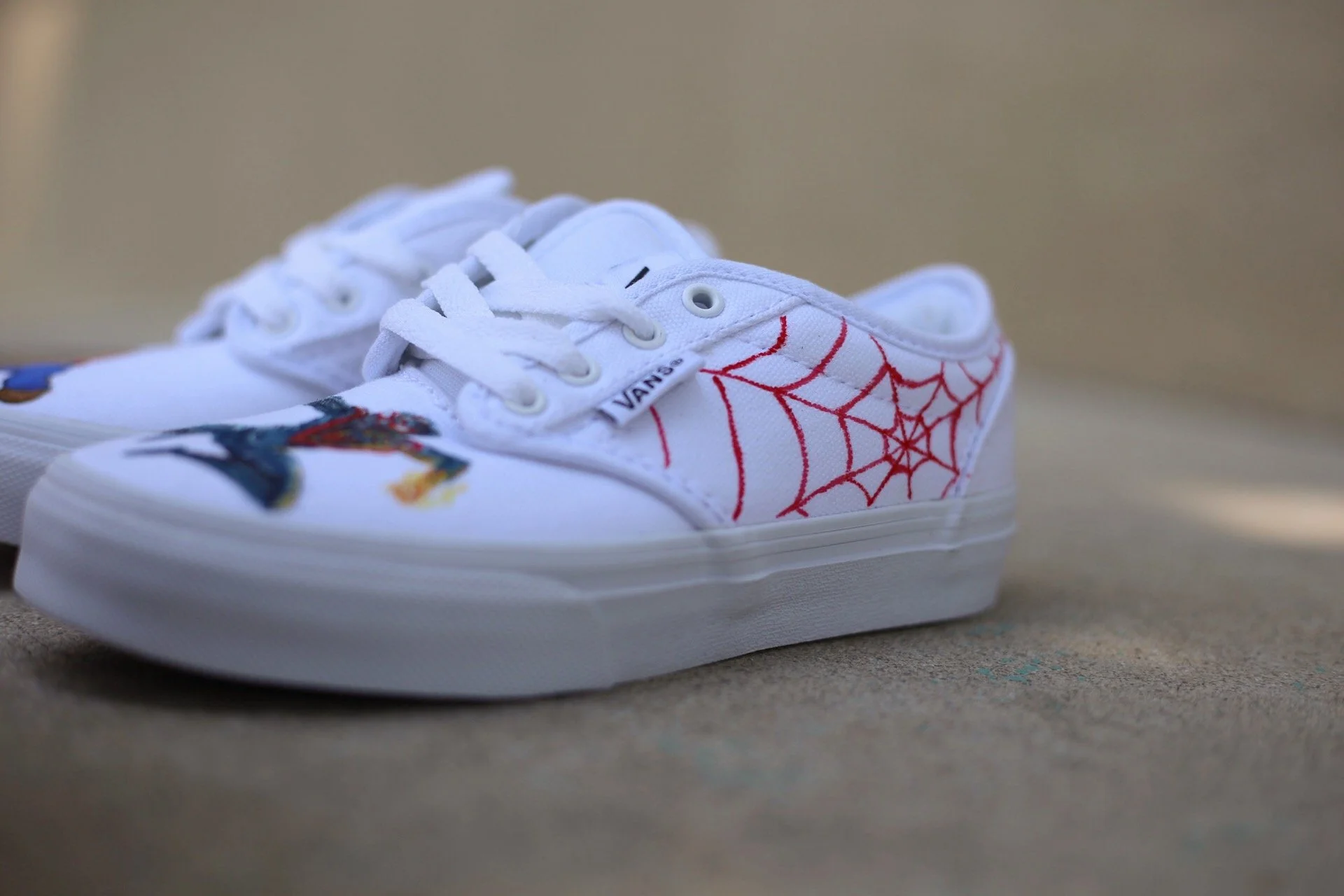 White sneakers with hand painted spiderman inspired red spiderwebs on the side and Spiderman painted on the toe. Hand painted children's shoes with well known children's characters. 