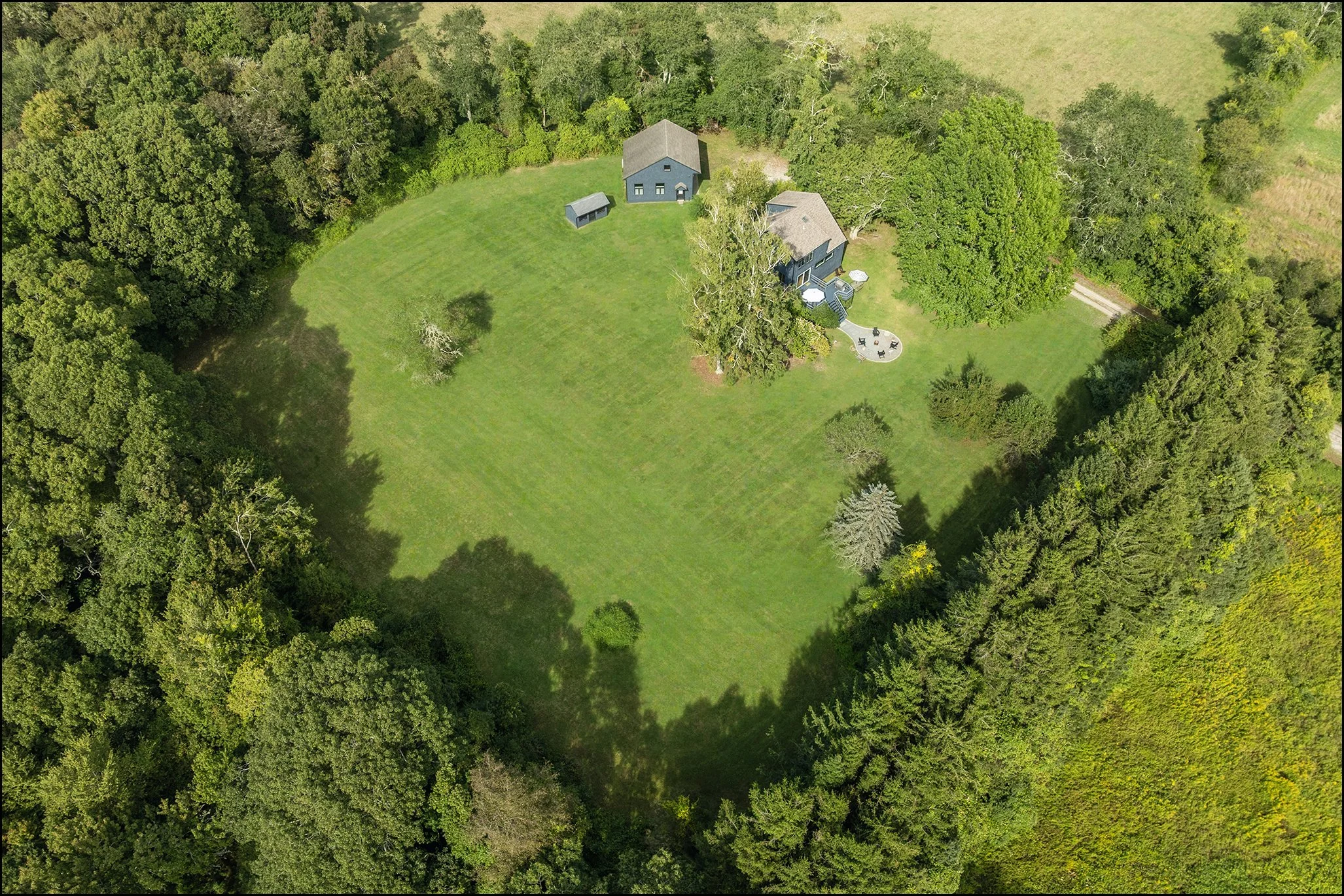 Aerial view of a house surrounded by a grassy yard and a dense forest.