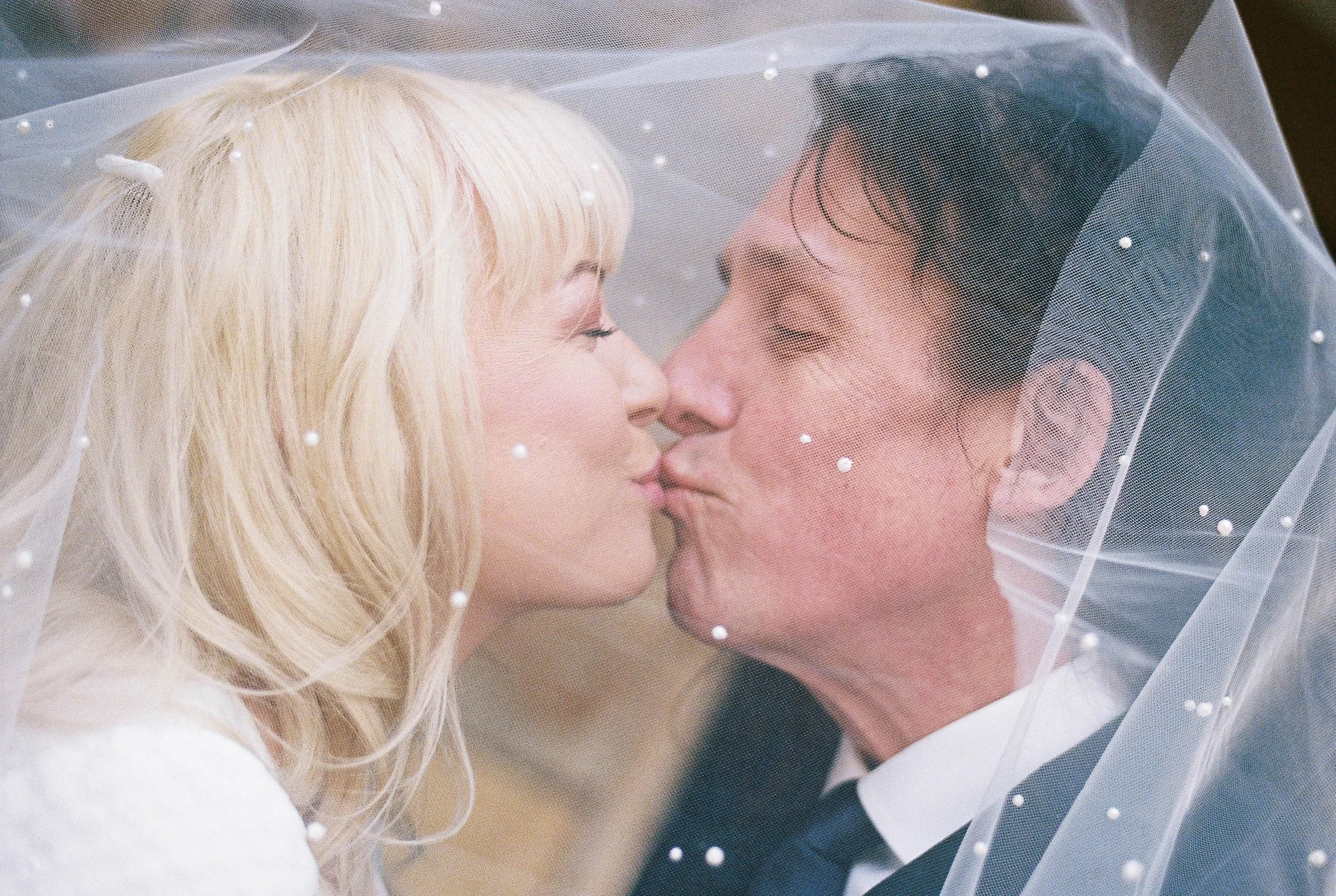 A bride and groom about to kiss under a veil, close-up of their faces.