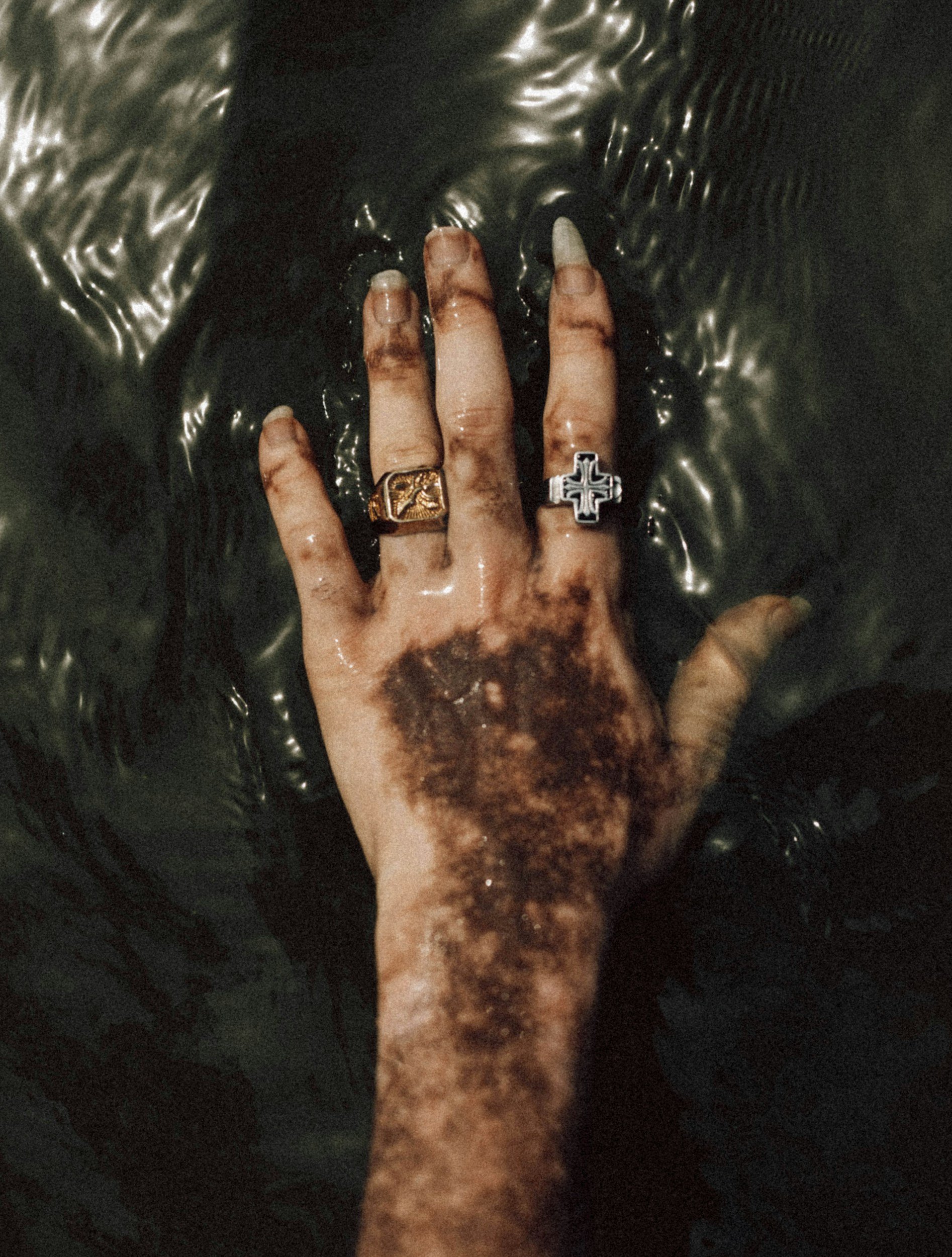 A close-up of a person's hand with rings, touching a shiny, textured black surface, possibly a metallic or plastic object.