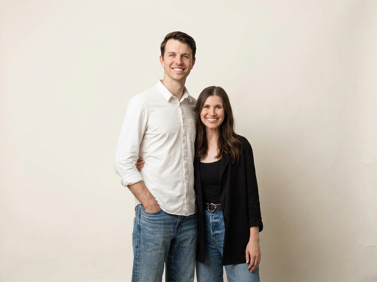 A smiling man and woman standing close together against a plain, light-colored background.