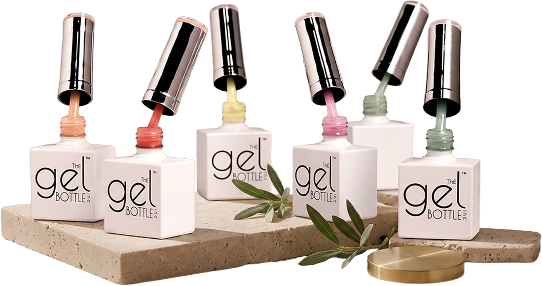 Six nail polish bottles with open caps on a stone slab, with some green leaves and a gold lid nearby.
