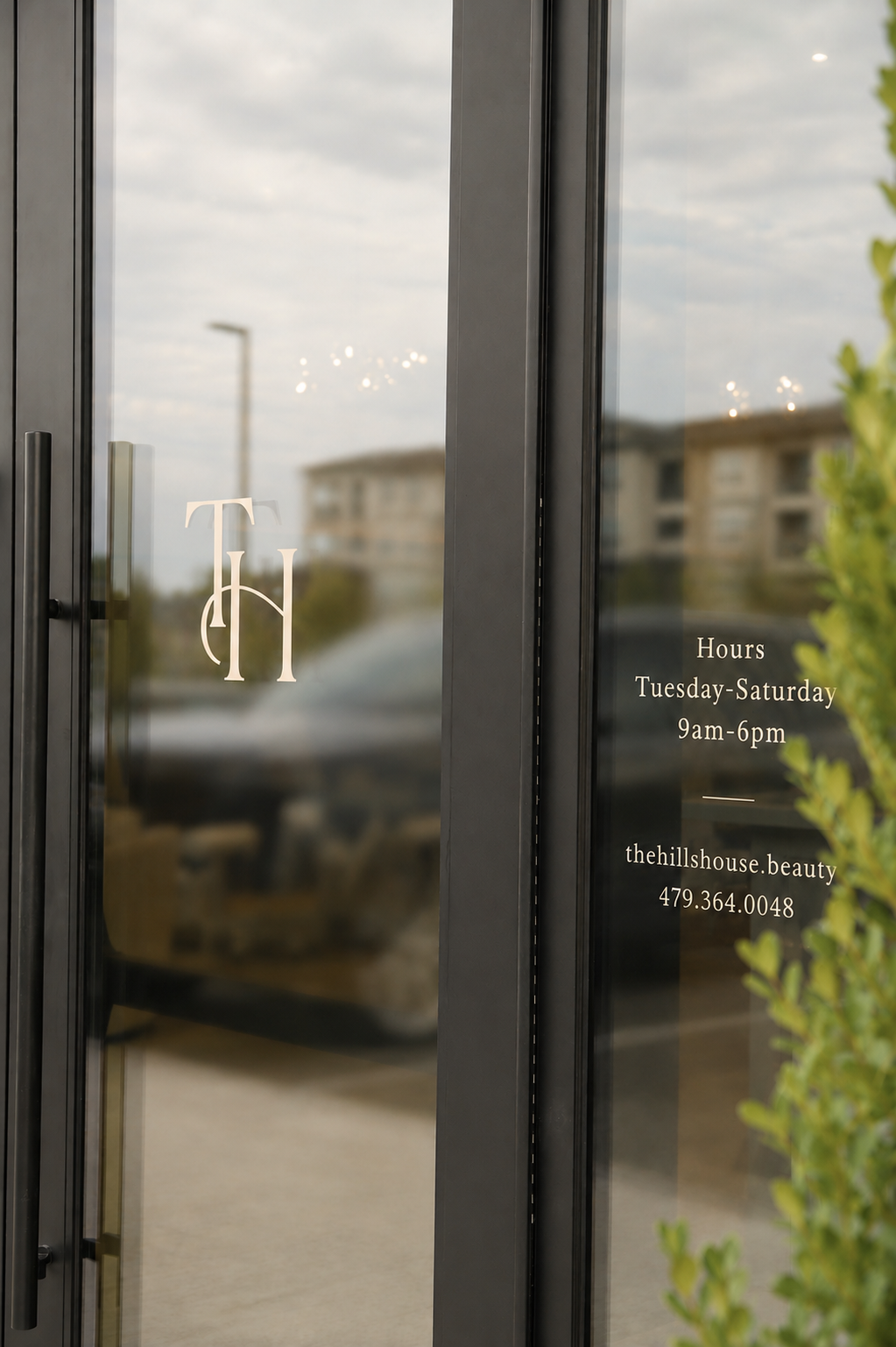 Glass door with business logo, hours, and contact information for The Hill House Beauty. Entering hours are Tuesday to Saturday from 9 am to 6 pm.