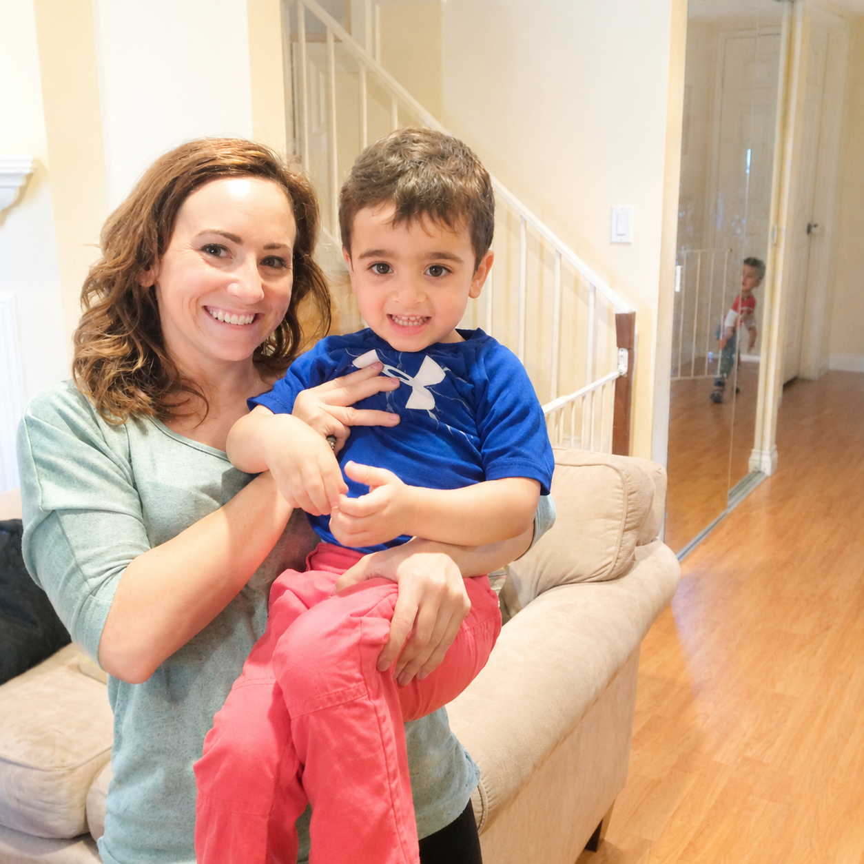 A woman with curly brown hair holding a young boy with short brown hair, both smiling, in a living room.  The child has finished speech therapy in California.