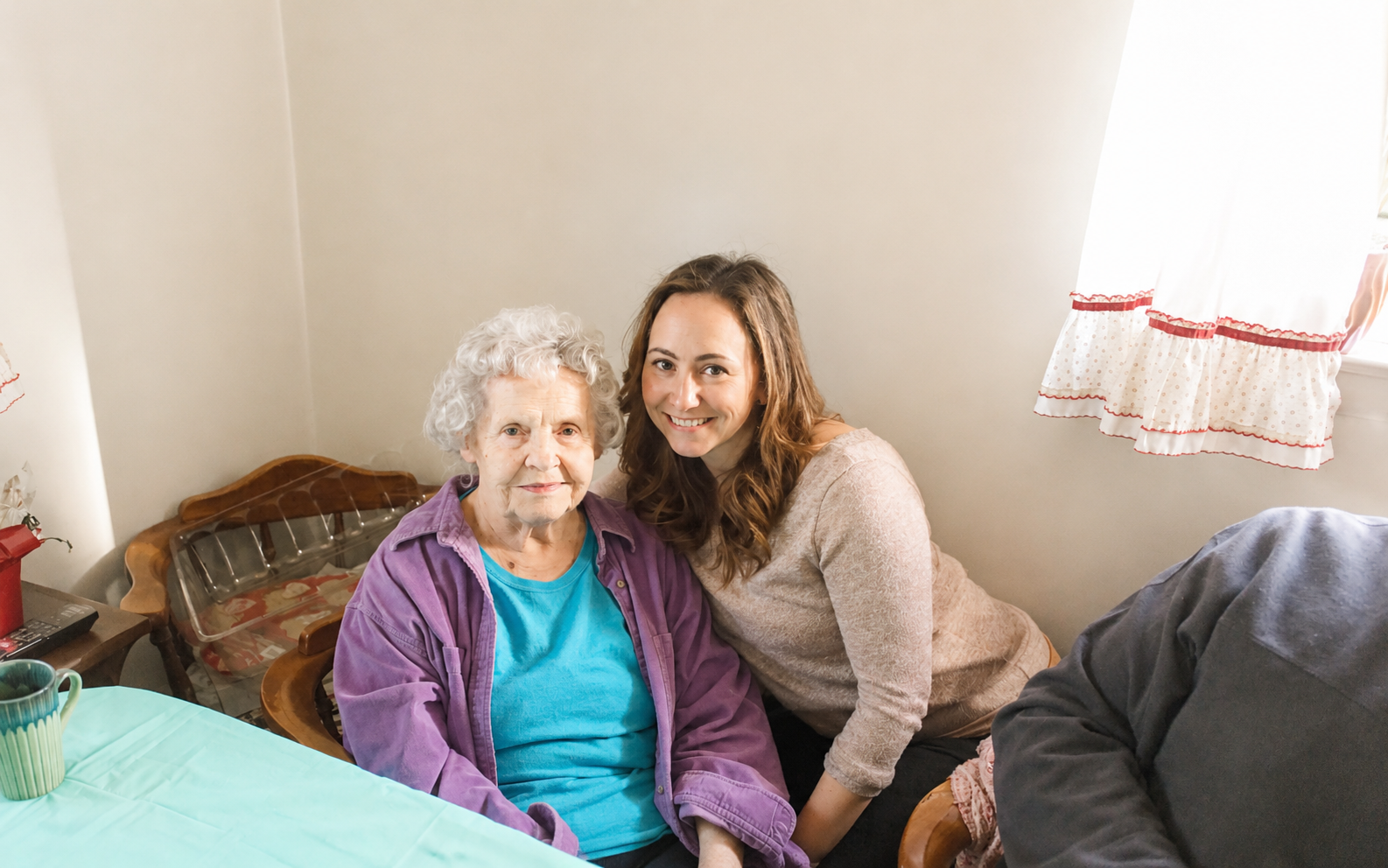 A smiling young woman and an elderly woman sit together at a table in a cozy room, after speech therapy in Savannah, GA.