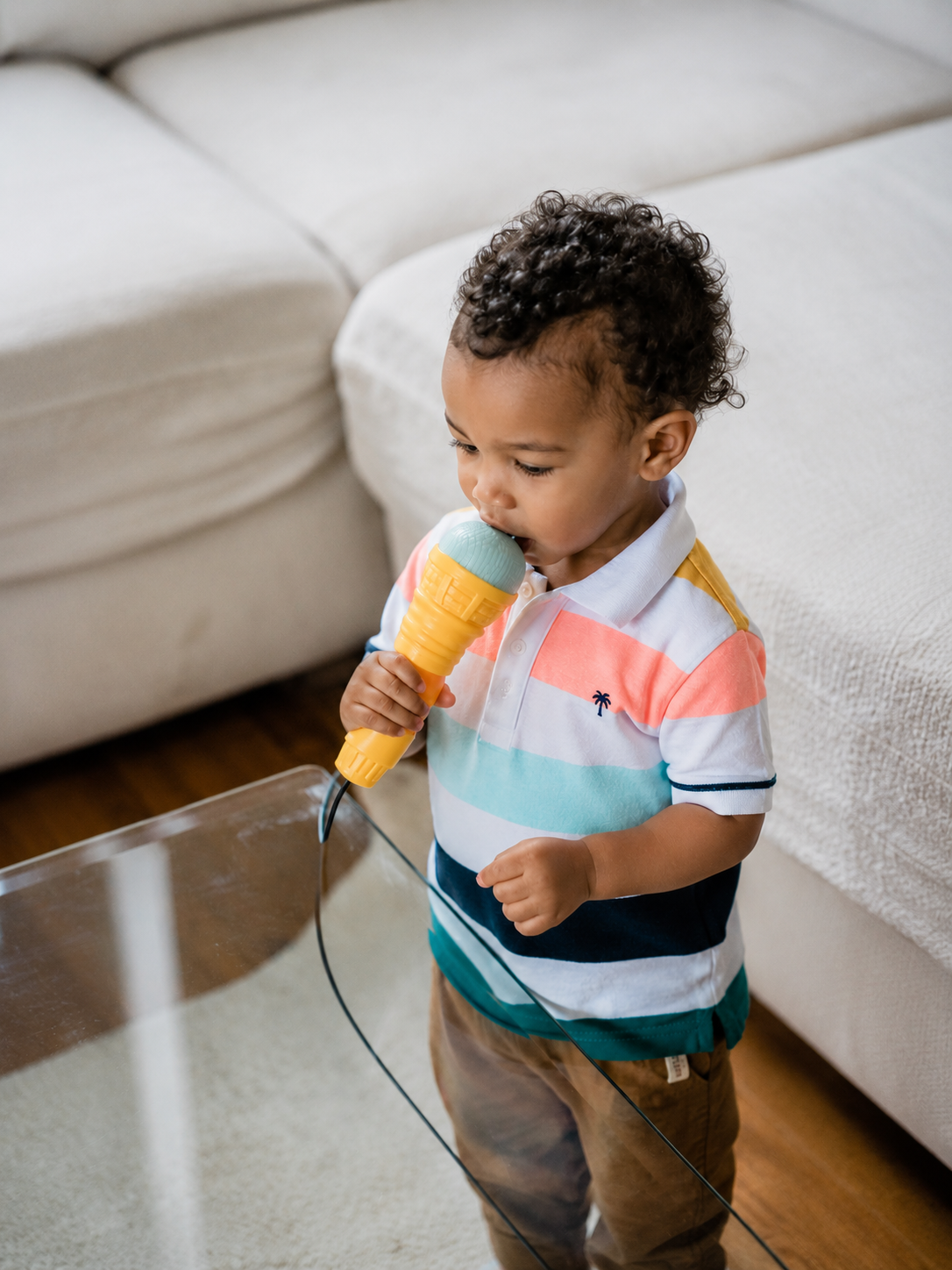 A young child with curly hair wearing a colorful striped shirt and brown pants, holding a micorophone as he learns to talk in speech therapy in Savannah, GA.