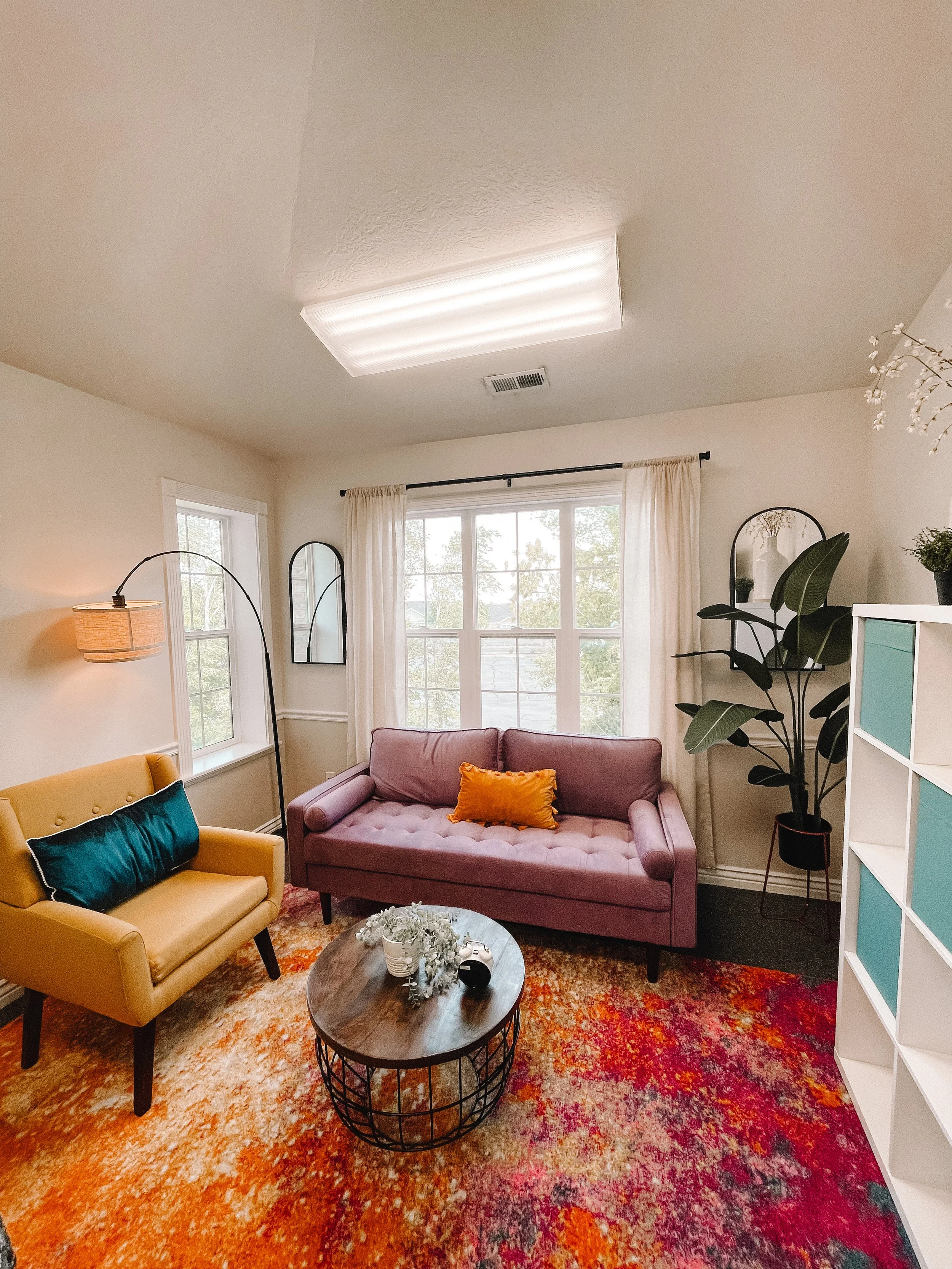 Therapy office with mauve couch, mustard armchair, and colorful area rug at Blue Bee Counseling