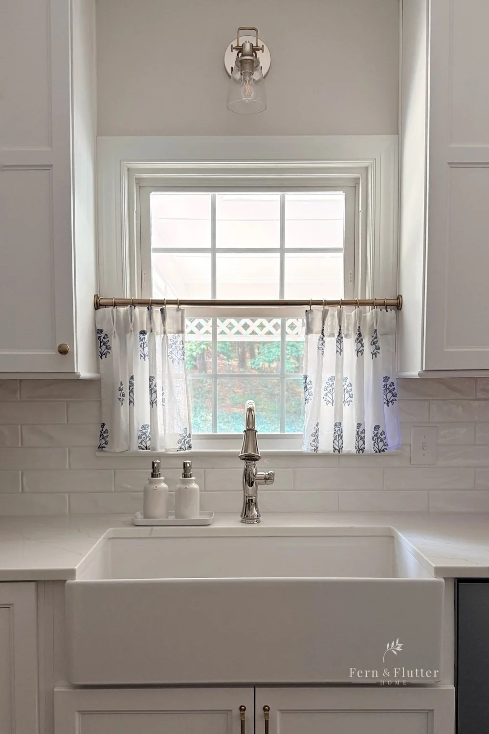 Café curtain hung in a bright white kitchen on a brass rod.
