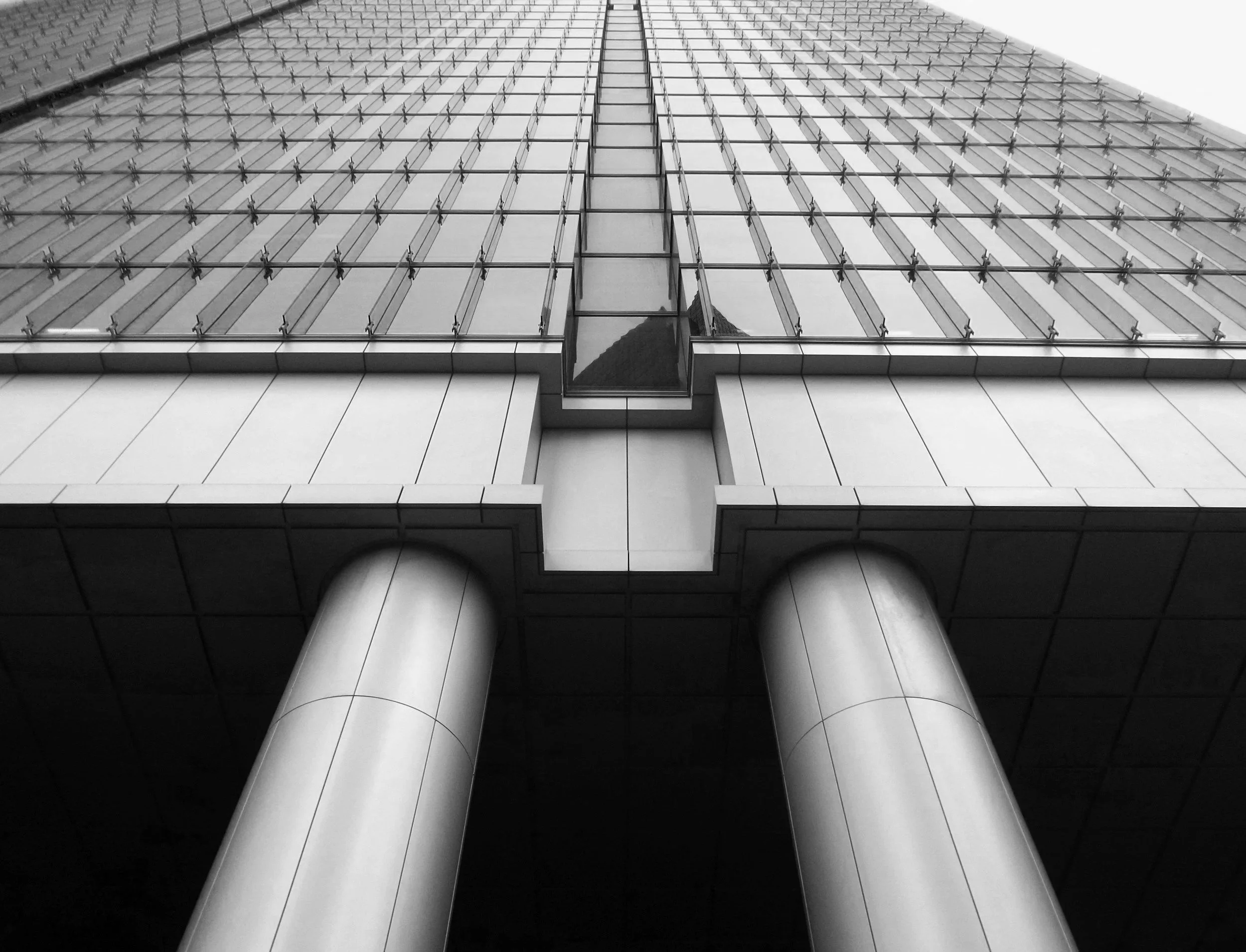 looking up at a modern glass skyscraper with reflective windows and metal framework, taken from the ground level