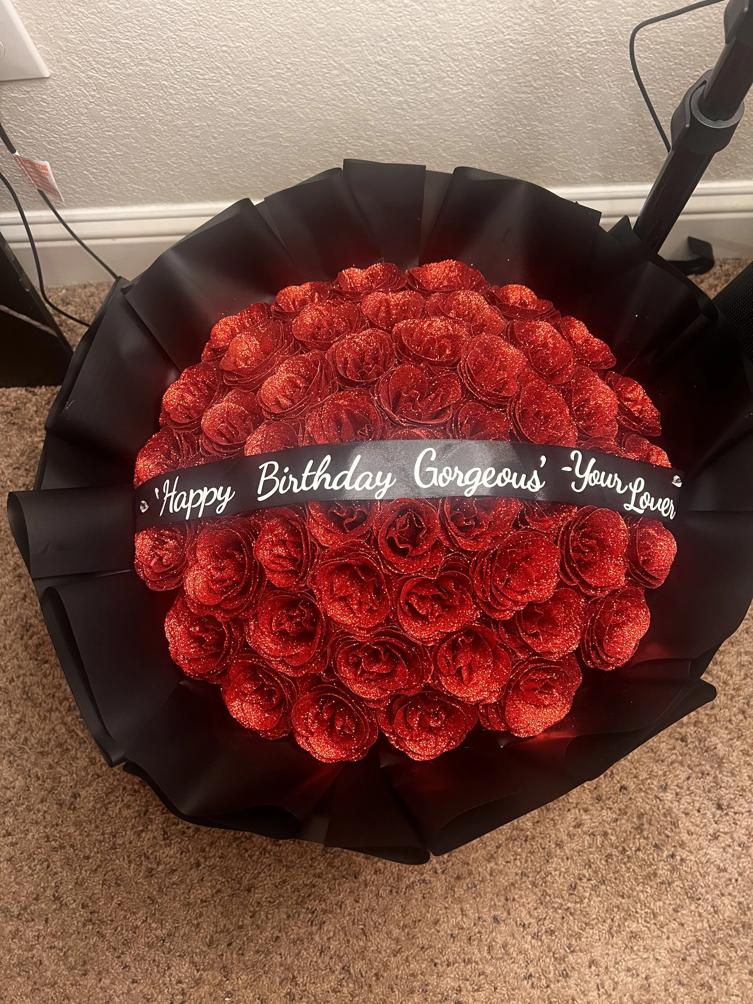 A bouquet of red roses with glitter, wrapped in black paper with a 'Happy Birthday Gorgeous' message.