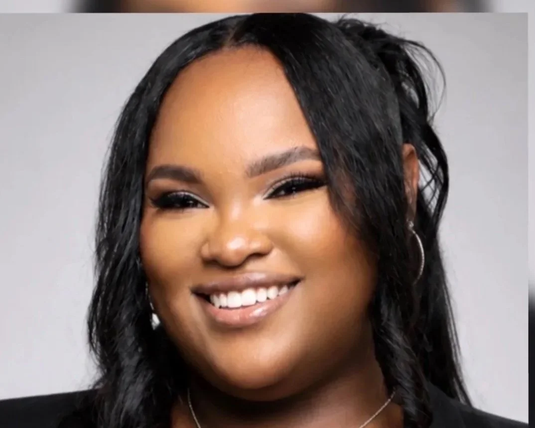 Close-up of a smiling woman with black hair, earrings, and makeup.