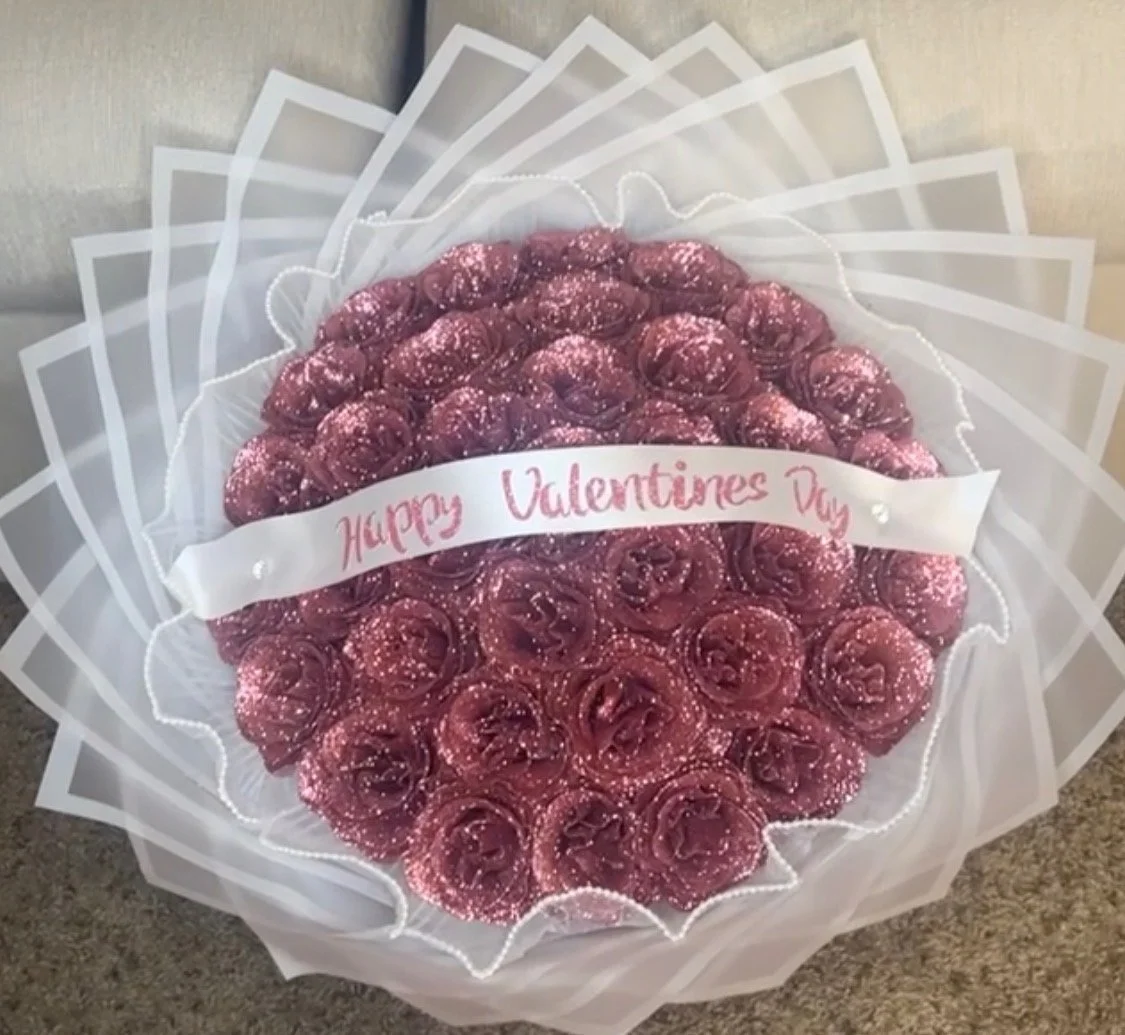 Heart-shaped bouquet of roses decorated with pink glitter and a ribbon that reads 'Happy Valentines Day'.