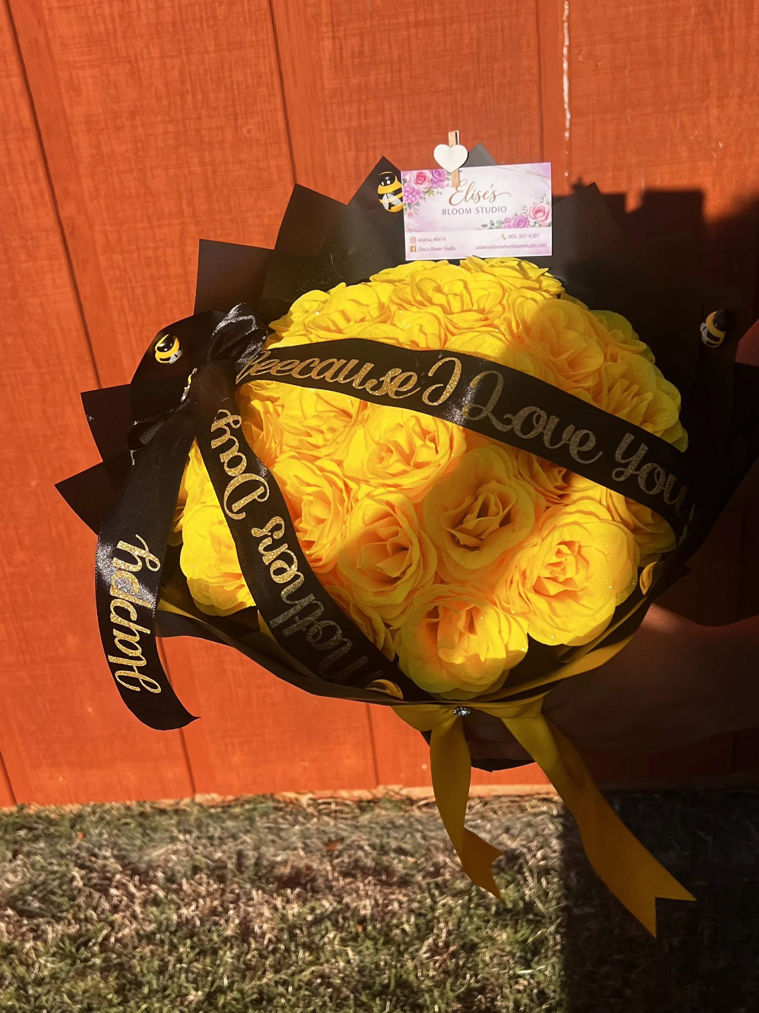 Yellow rose bouquet with black ribbon that reads 'Specially Love You' held in front of a red wooden wall.