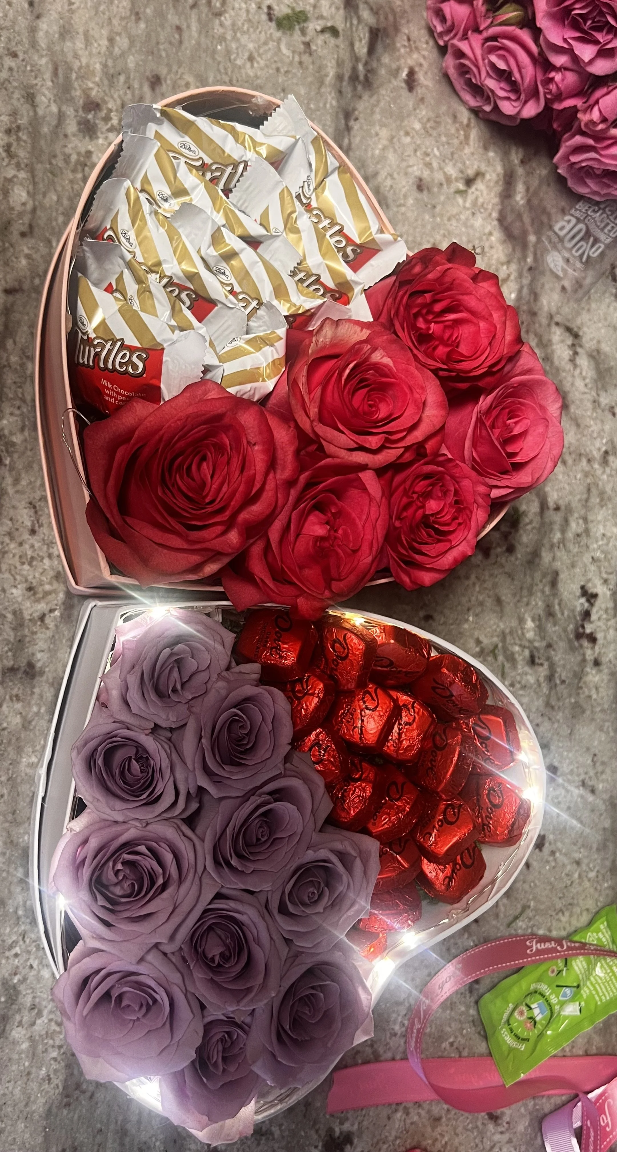 Heart-shaped boxes with roses and chocolates, including purple, red roses, and assorted candies on a countertop.