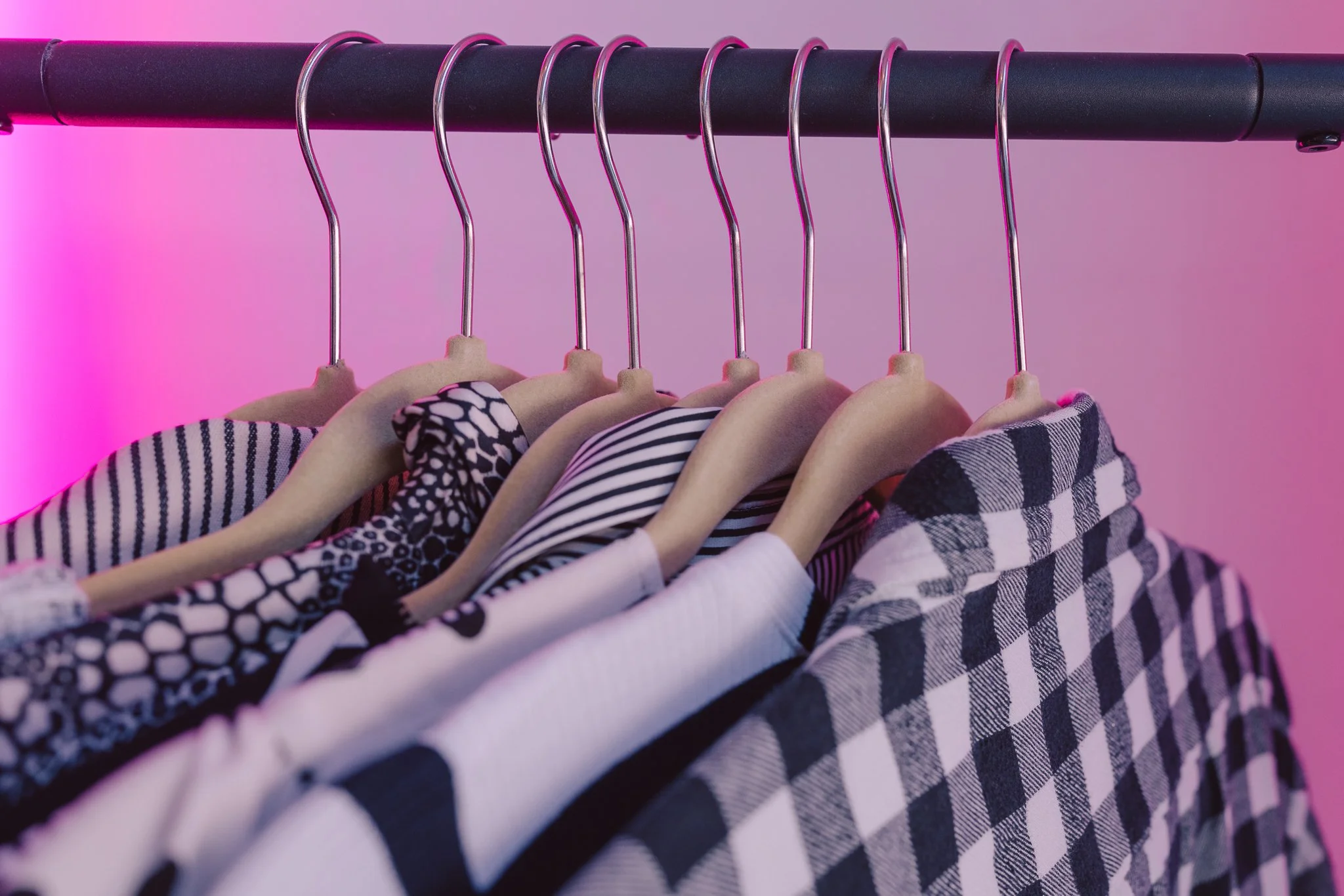 Clothing items hanging on pink hooks on a black rod with a pink background.