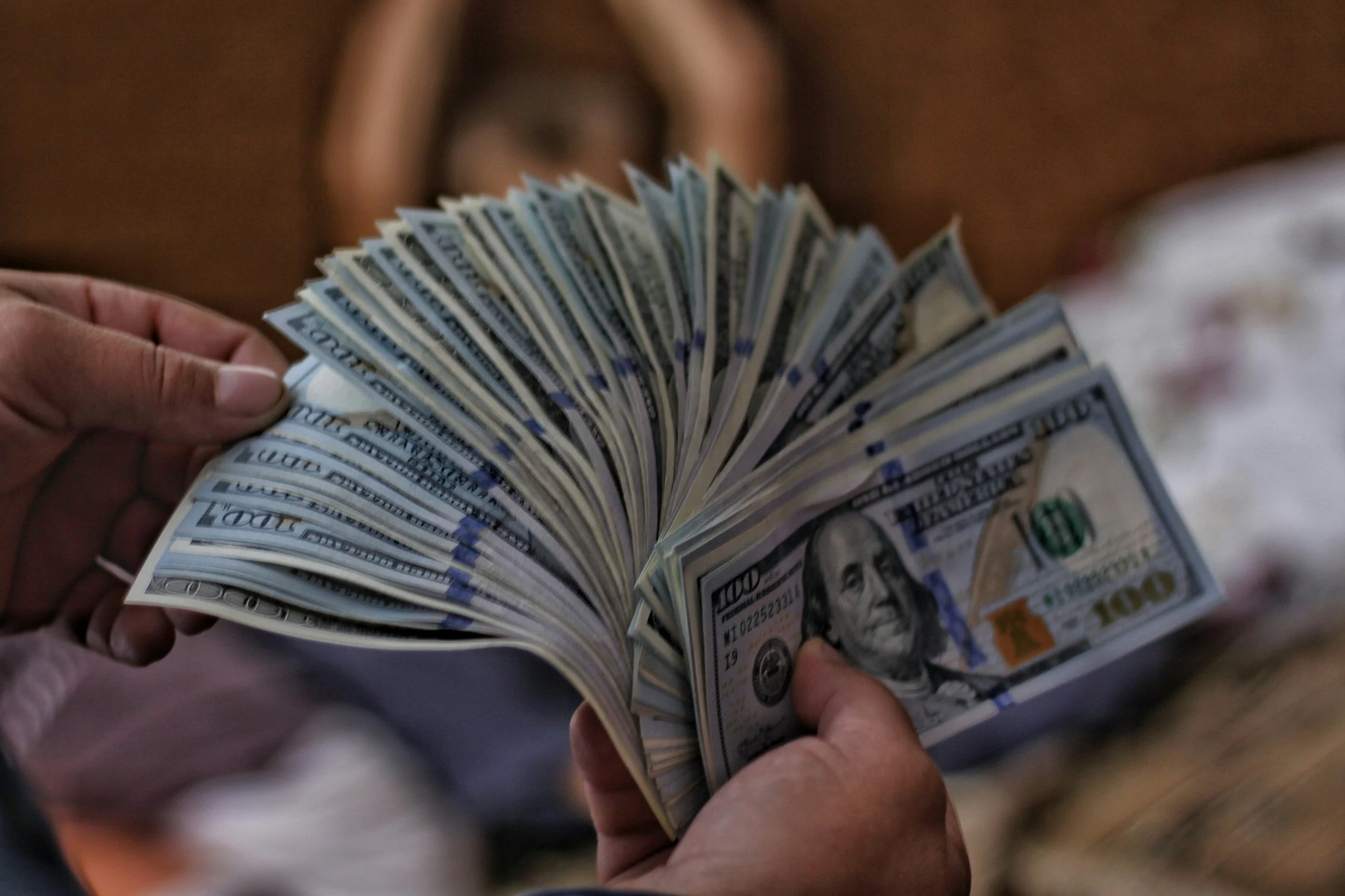 Close-up of hands holding a fanned stack of US $100 bills.
