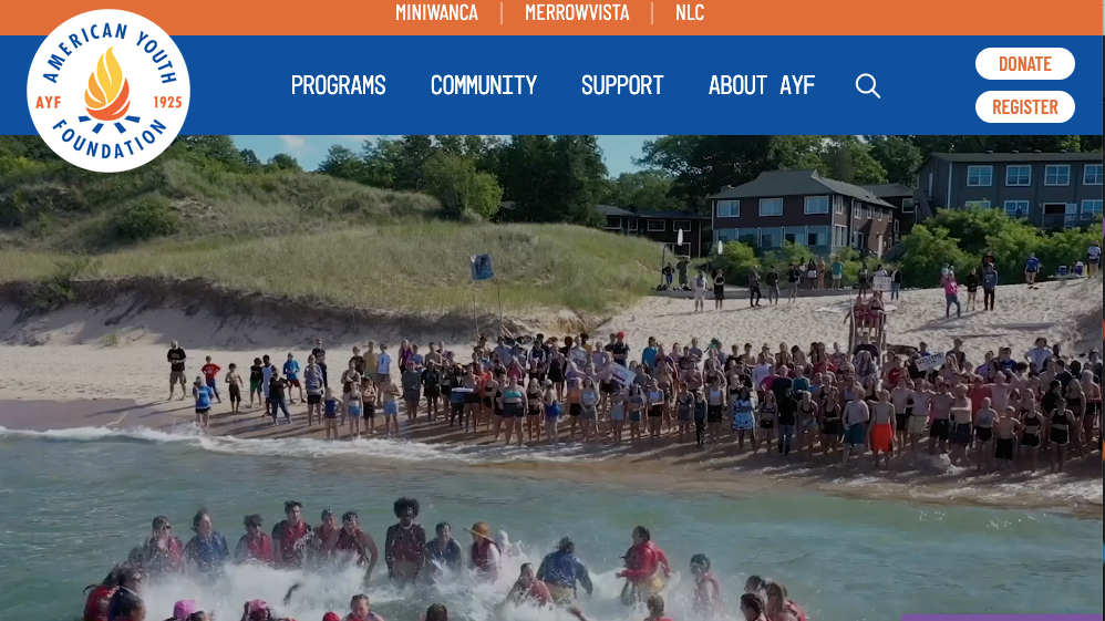 A screenshot of a website landing page with an orange and blue menu bar and an image of a group of people gather on a beach near the water, with some in the ocean and others on the sand. T