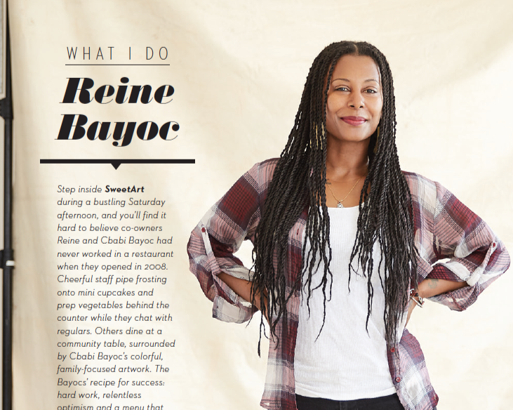 A woman with long braids wearing a plaid shirt and white top, standing with her hands on her hips.