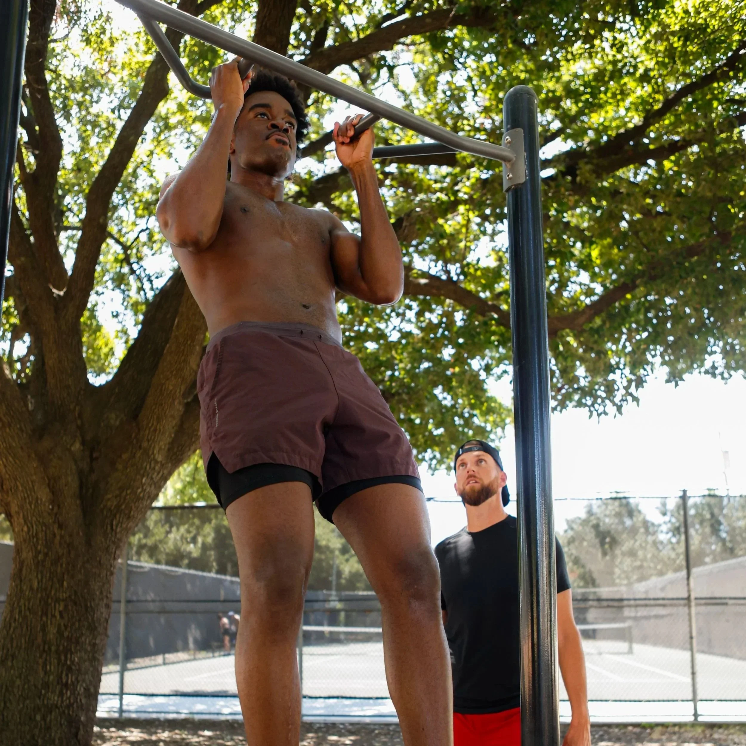 Samuel "S3" Arnold III doing pull-ups outdoors as Coach Andrew Banner looks on during a fight camp strength and conditioning session.