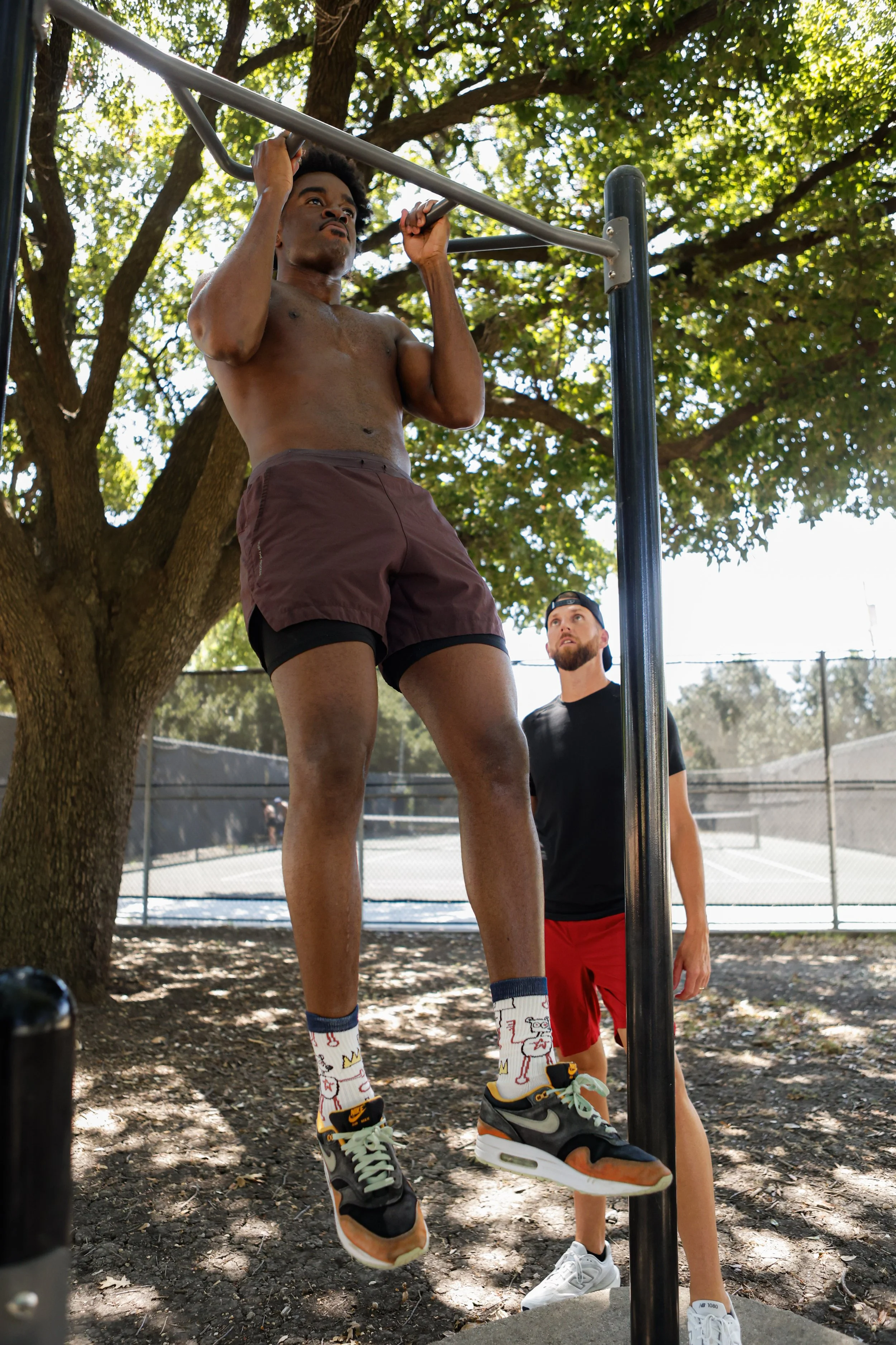 Samuel "S3" Arnold III doing pull-ups outdoors as Coach Andrew Banner looks on during a fight camp strength and conditioning session.