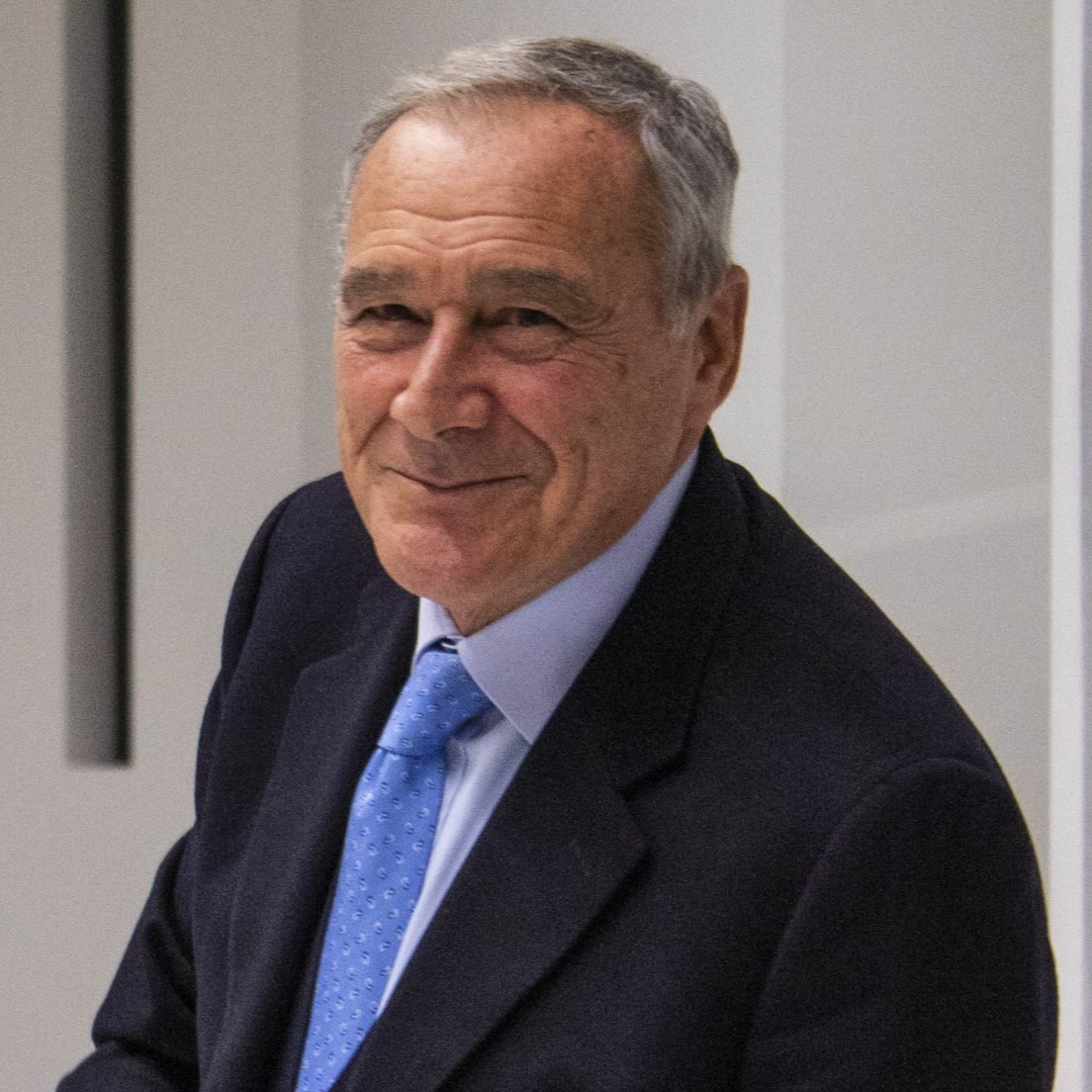 An older man in a suit with a blue tie smiling.