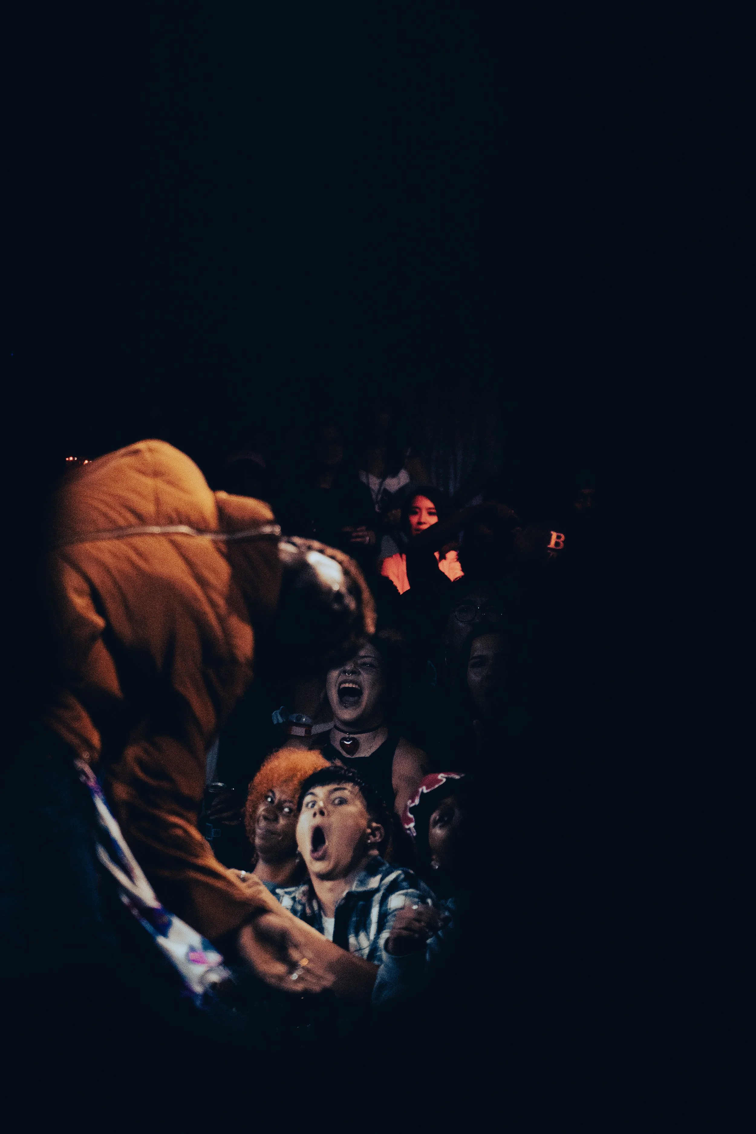 A crowd of people at night, some looking upward and expressing surprise or excitement, with dark sky overhead.